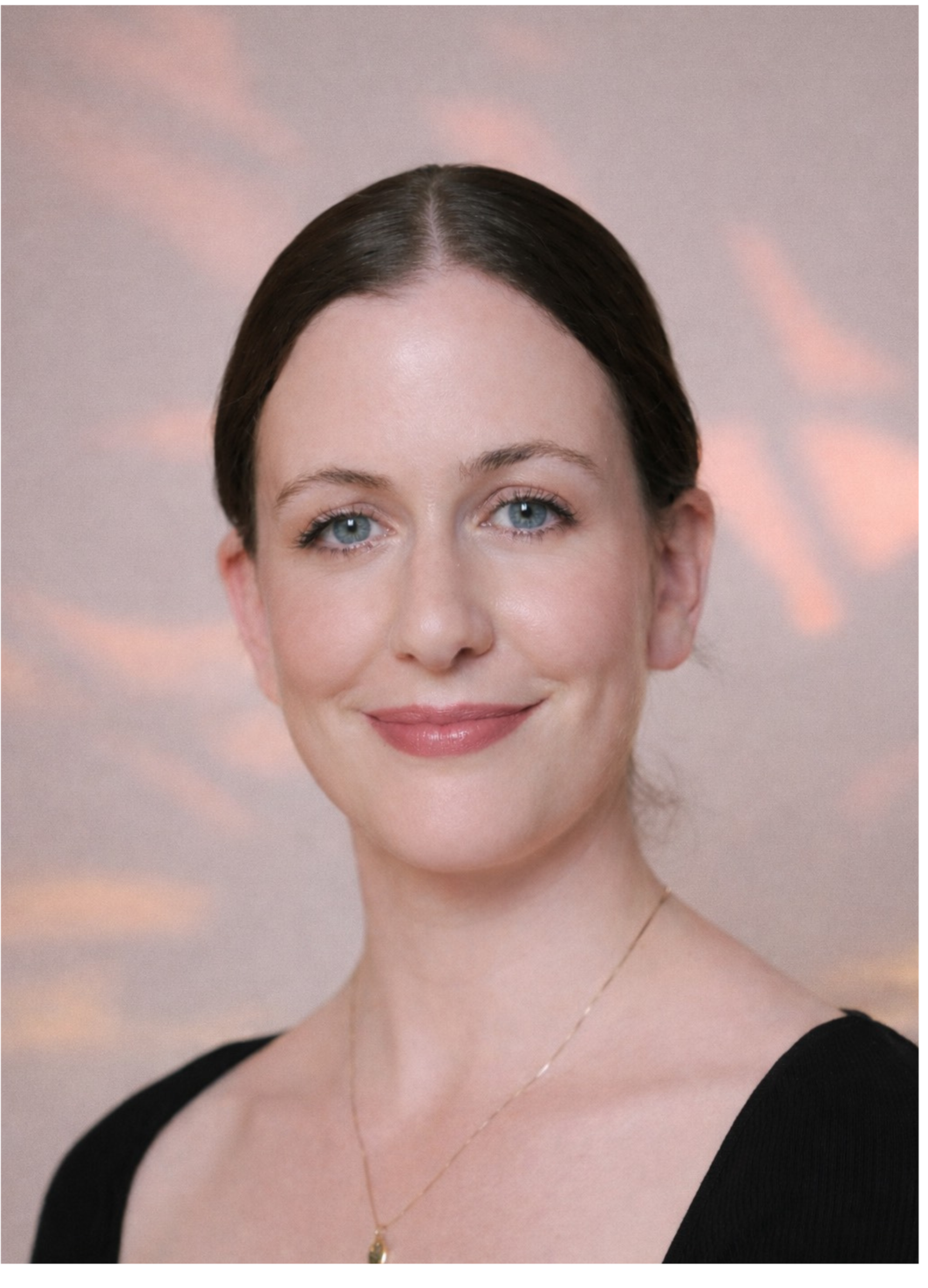 A woman with dark hair, dressed in a black sleeveless top, standing indoors with large green leaves of a Monstera plant beside her, against a light-colored wall.