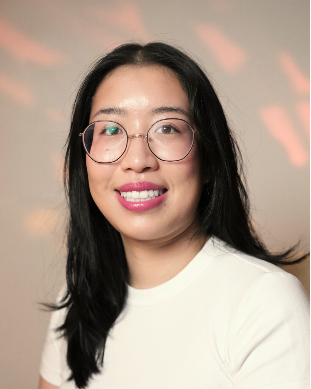 A woman with glasses and red lipstick smiling, with a large monstera plant behind her.