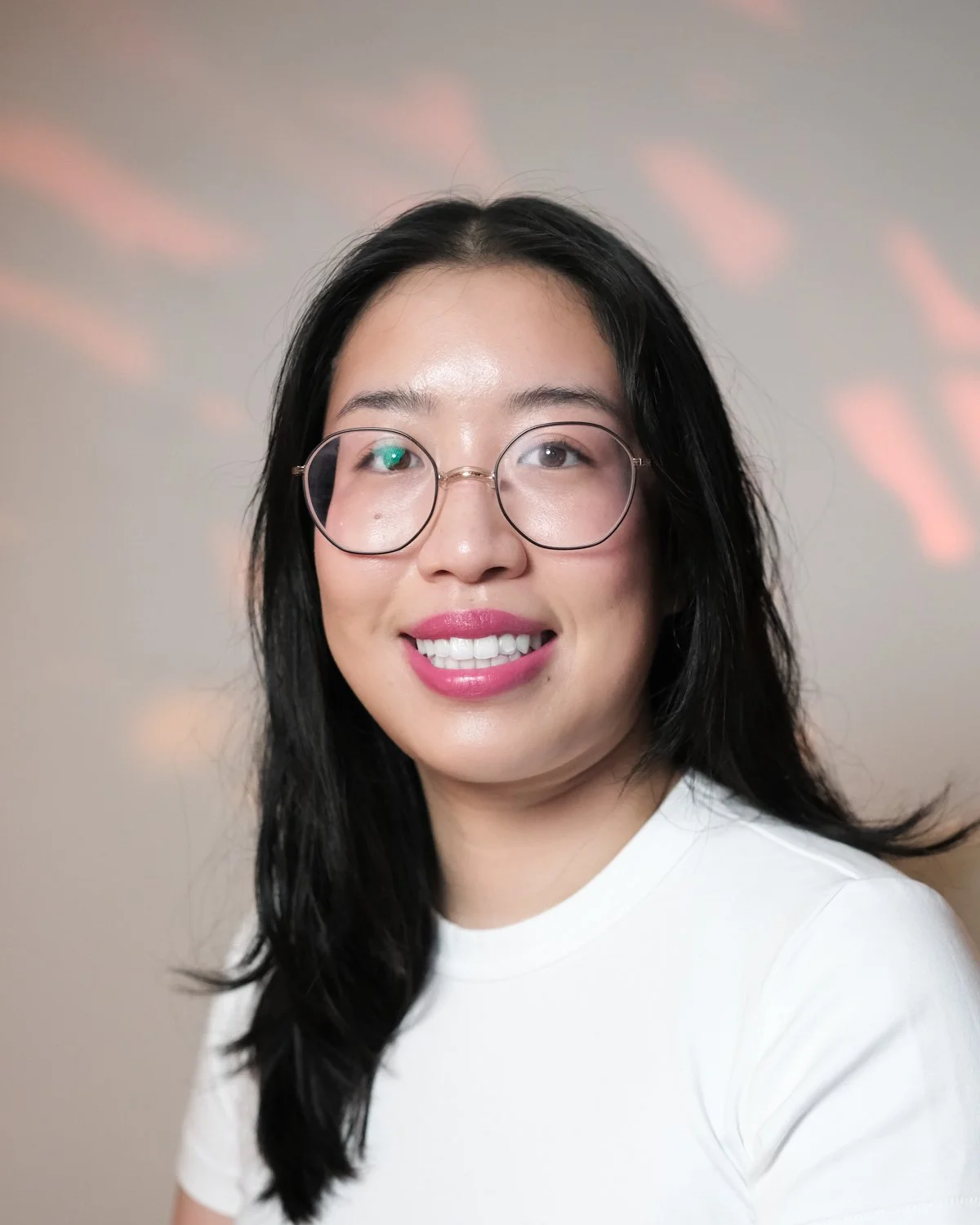 A woman with glasses and red lipstick smiling, with a large monstera plant behind her.