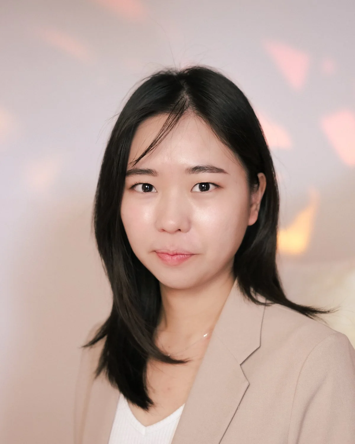 Young woman with long dark hair, glasses, and a gray University of Toronto sweatshirt smiling with arms crossed, standing next to a large green monstera plant against a plain light-colored background.