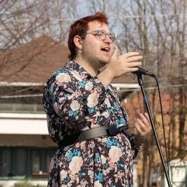Steven leading song with a dark floral dress in front of a microphone outside