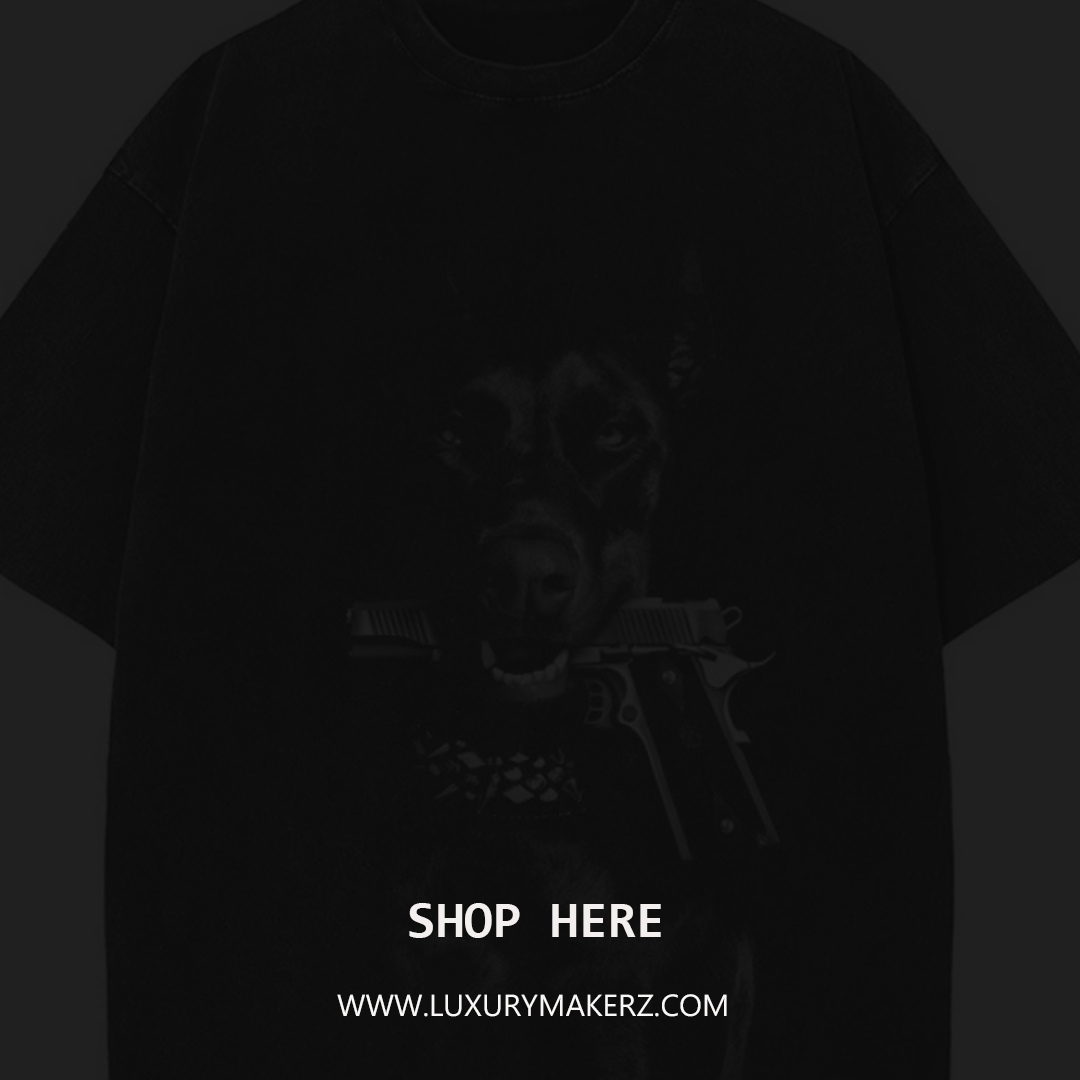 Dark-colored T-shirt with a graphic of a dog's face holding a gun in its mouth, and text that says "SHOP HERE" and "WWW.LUXURYMAKERZ.COM" at the bottom.