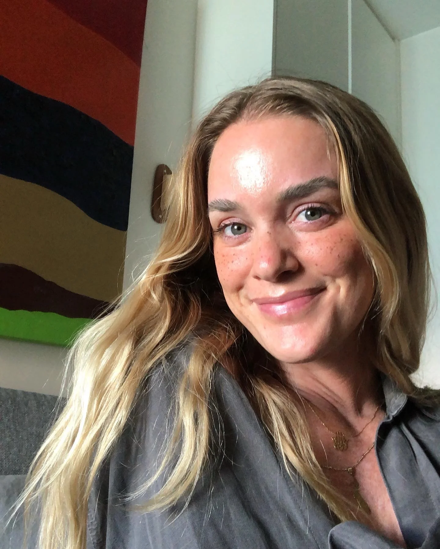 A woman with long blonde hair and freckles, smiling at the camera in a close-up selfie.