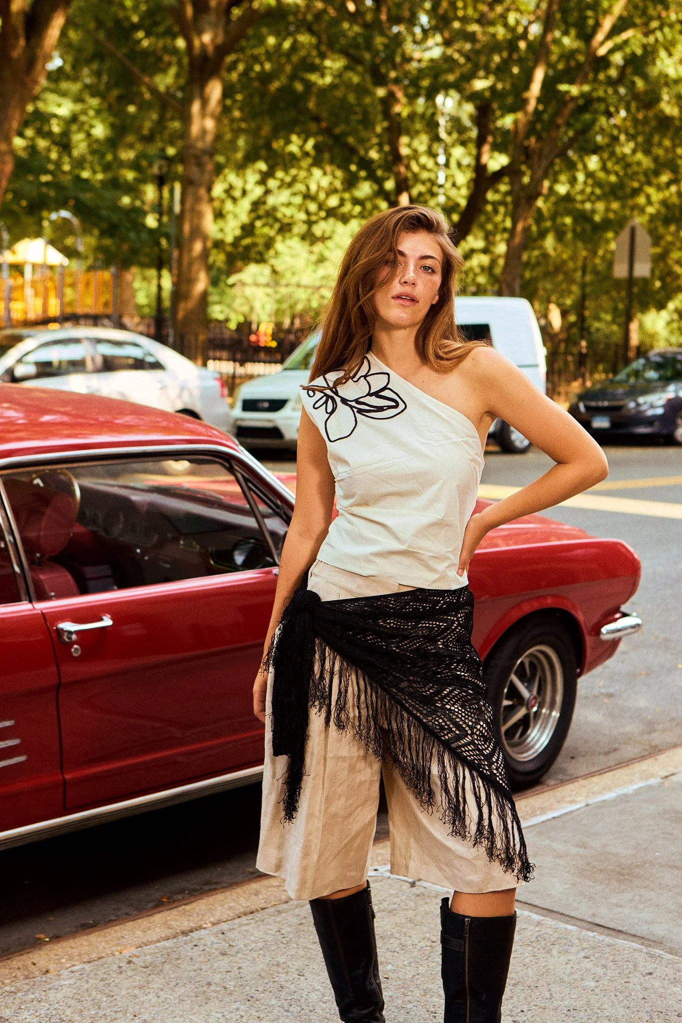 A woman stands in front of a red car.
