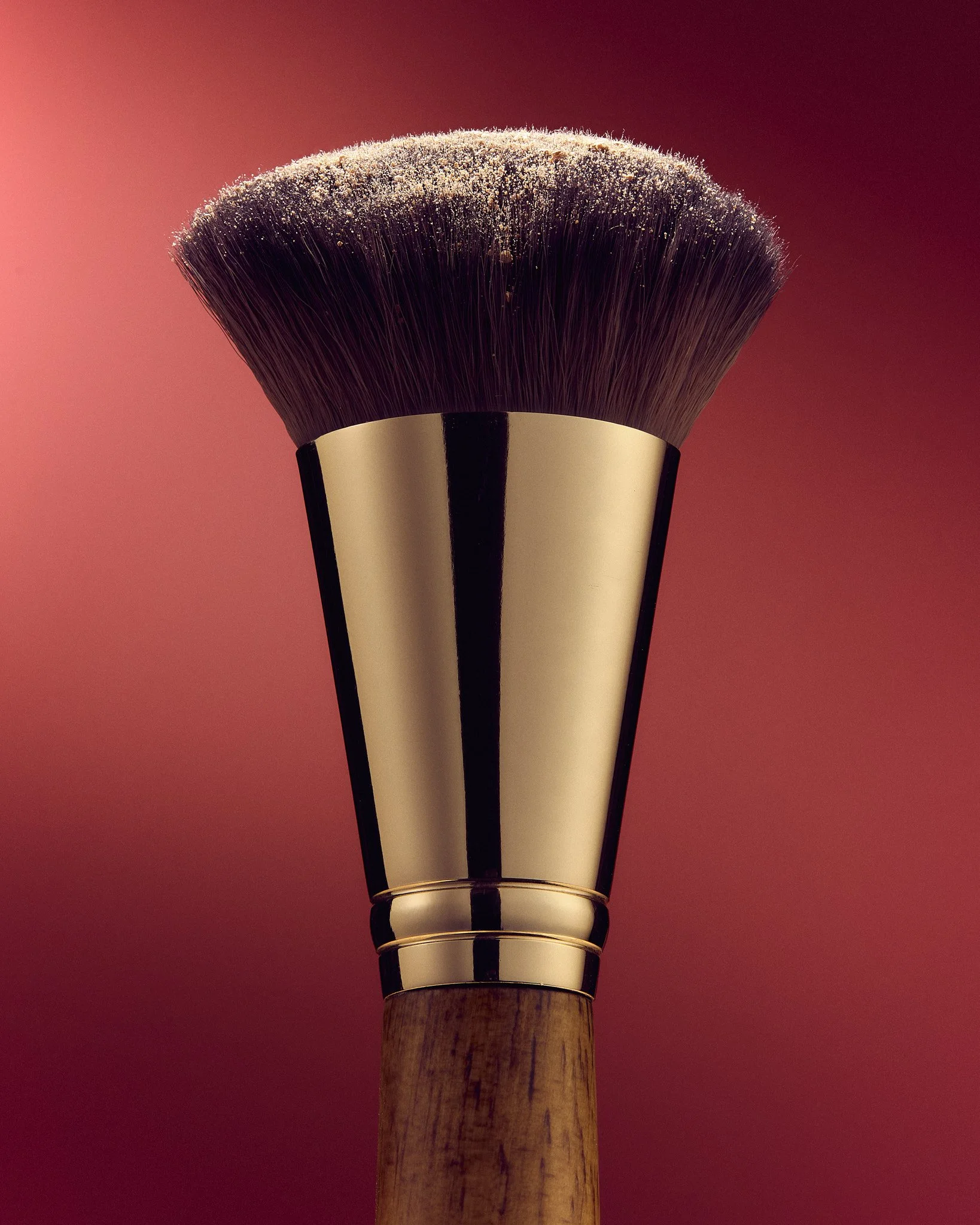 Close-up of a makeup brush with dark bristles and wooden handle against a red background.