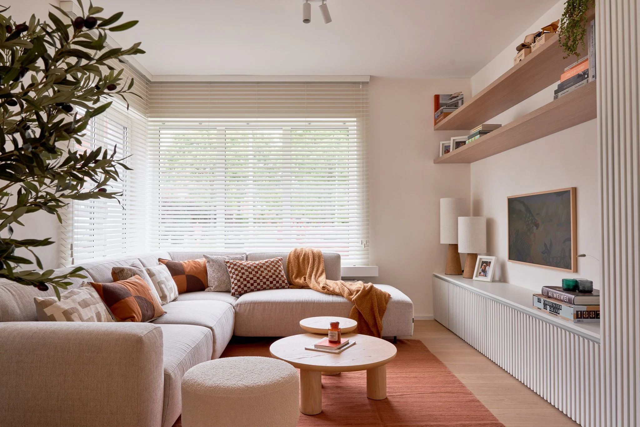 Woonkamer met lichte hoekbank, ronde salontafels en een maatwerk wandkast met verticale lamellen en eiken planken