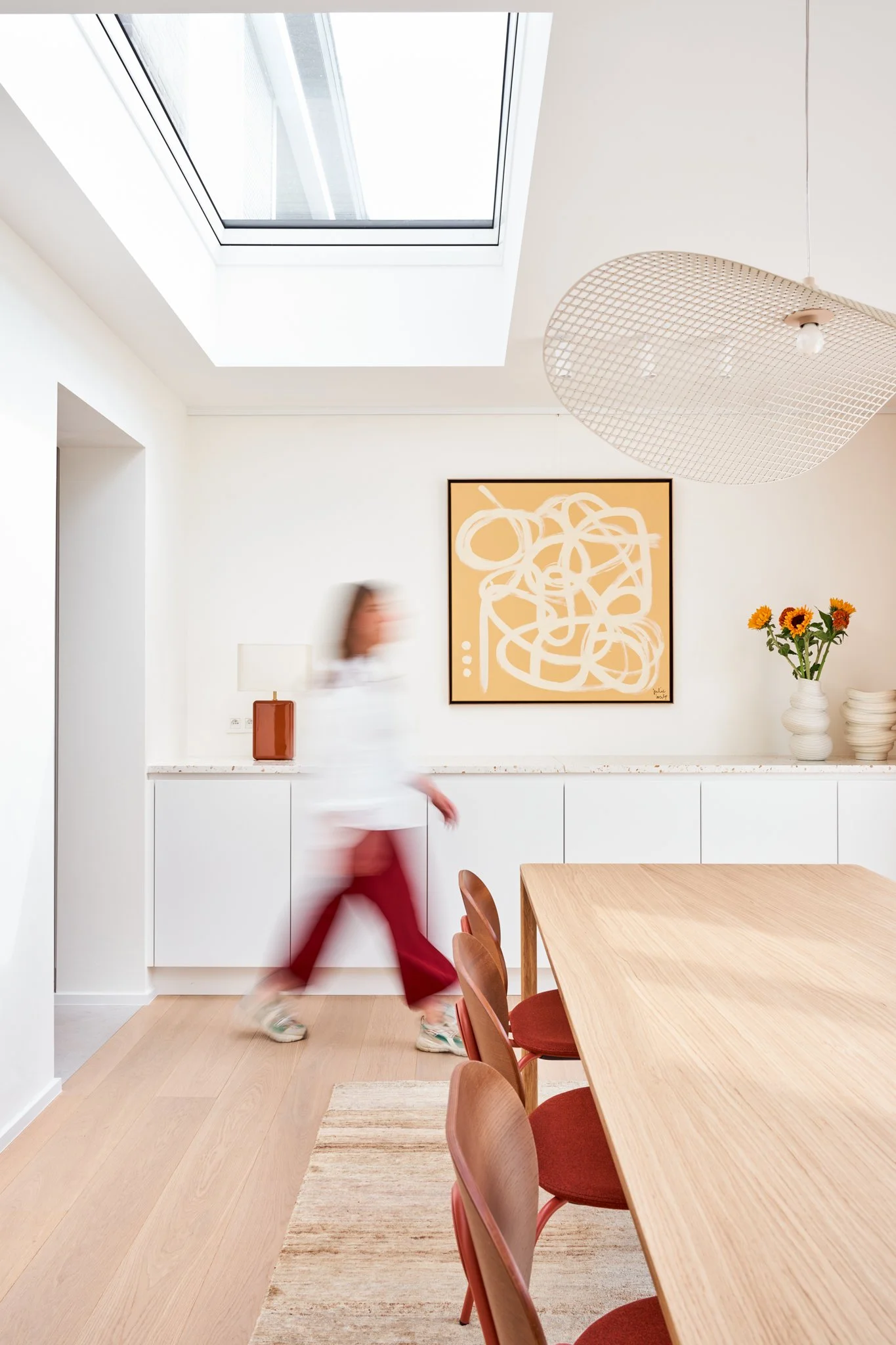 Lichte eetkamer onder een dakkoepel, met eiken tafel, roestbruine stoelen en witte kasten met terrazzo blad