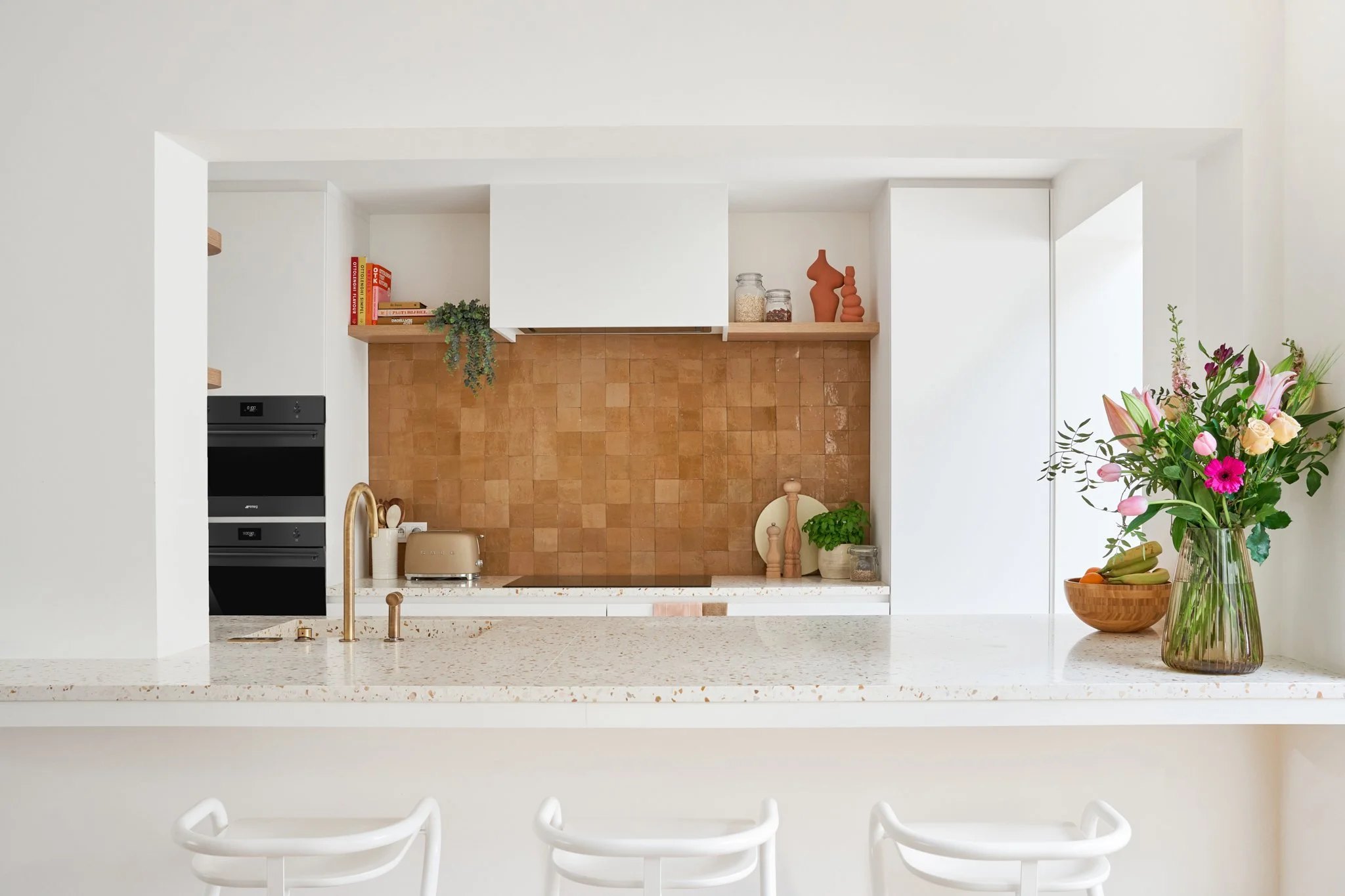 Open keuken met okerkleurige zelliges als achterwand, messing kraan en terrazzo werkblad met barkrukken