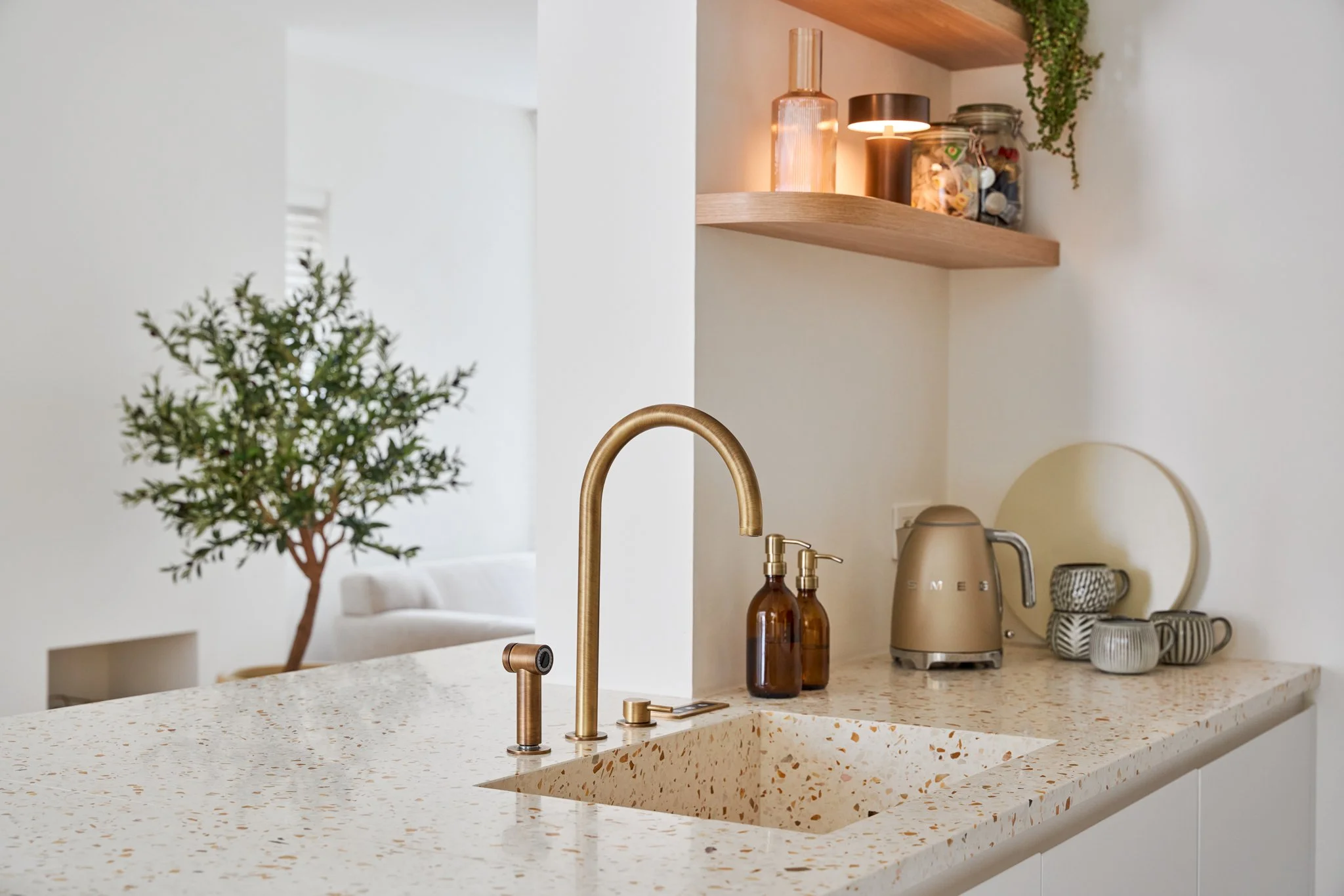 Terrazzo werkblad met geïntegreerde spoelbak, messing kraan en eiken wandplank in de keuken