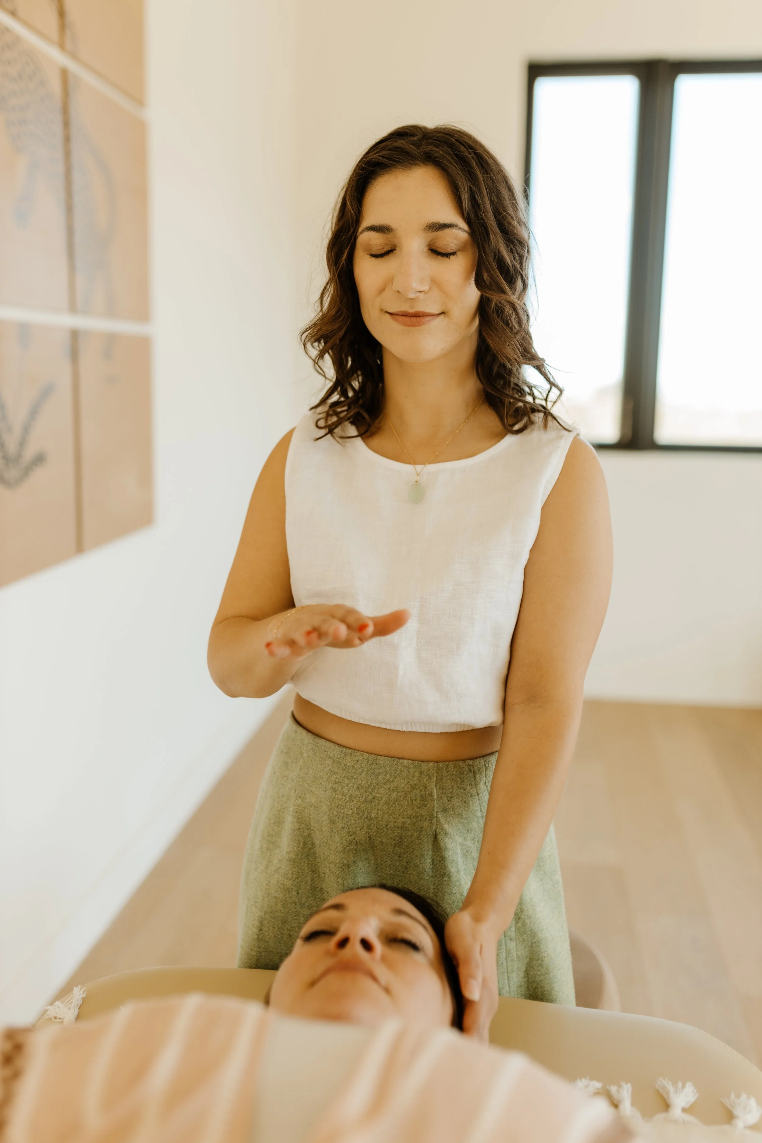 A woman receiving a healing or energy massage from a therapist in a calming room.