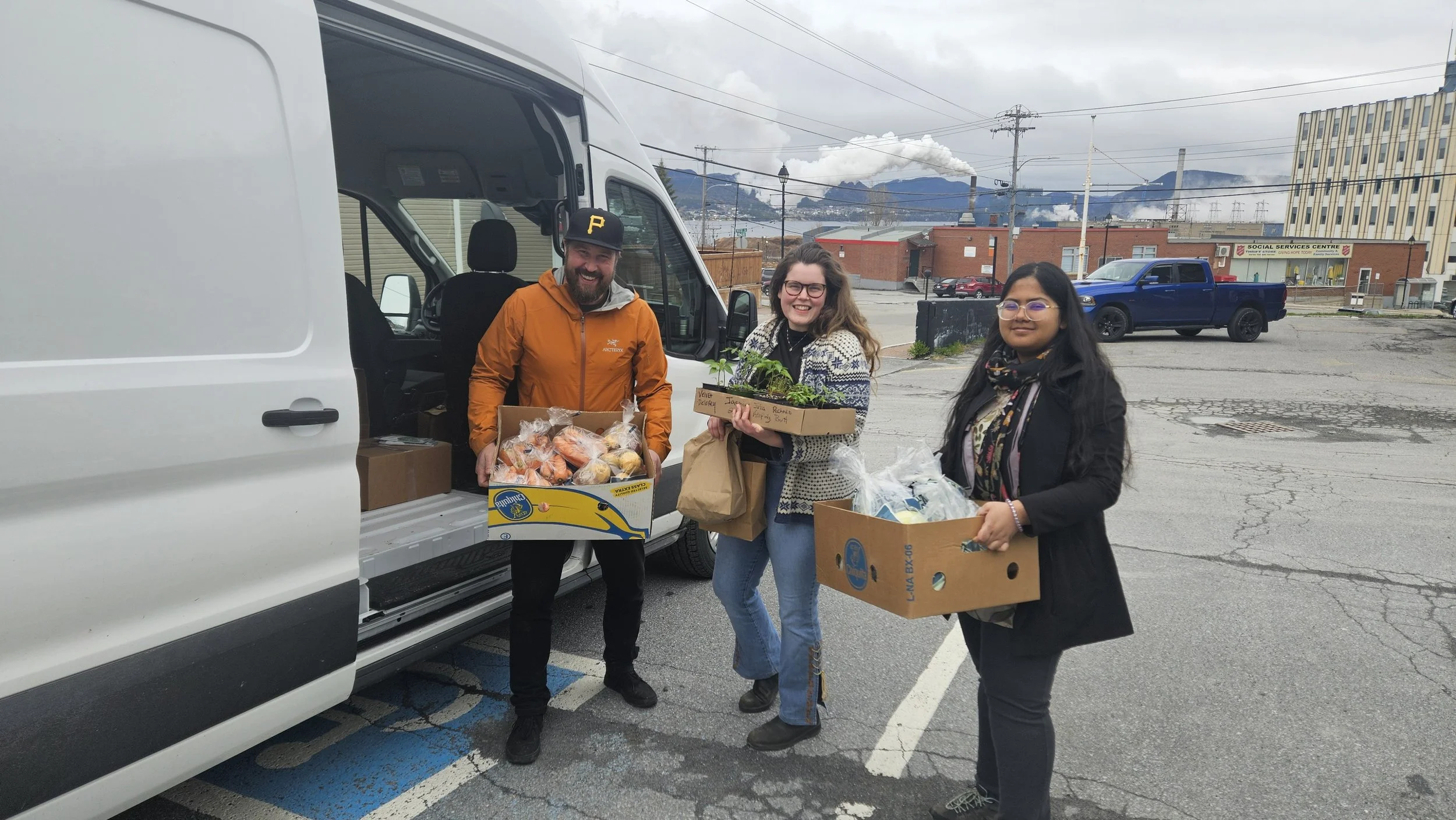 Three people holding boxes of produce standing by an open van