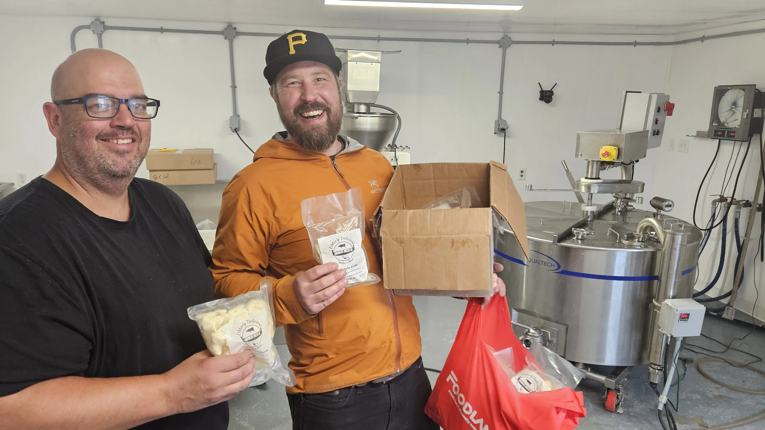 Two people holding up packs and a box of cheese