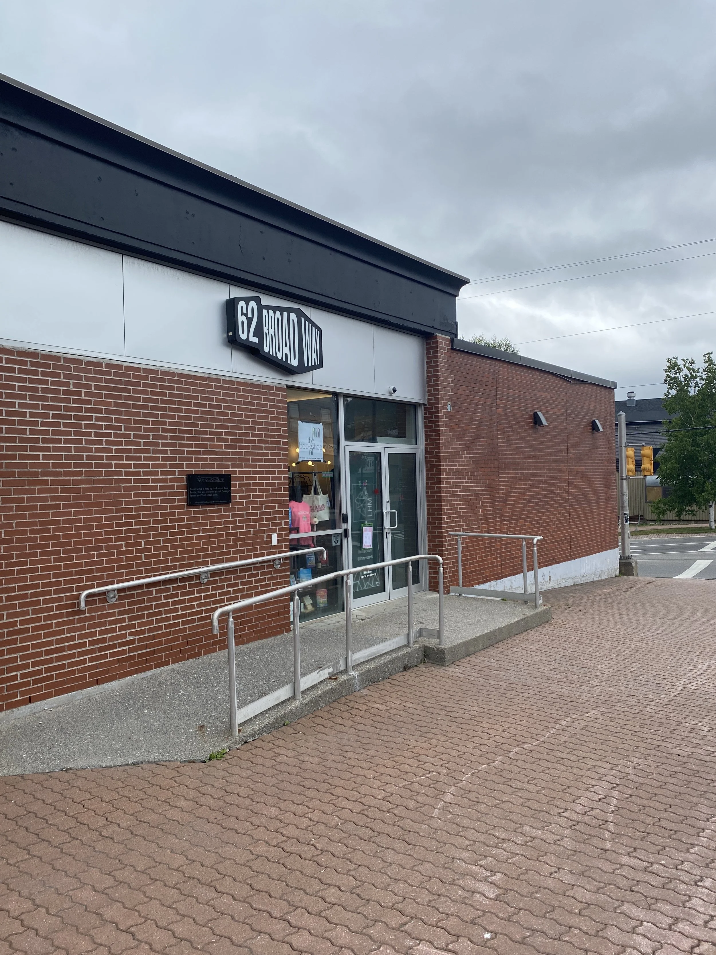 A view of the accessible side entrance at 62 Broadwayt, a brick building with glass doors and showcase window. A ramp leads to the door from left.