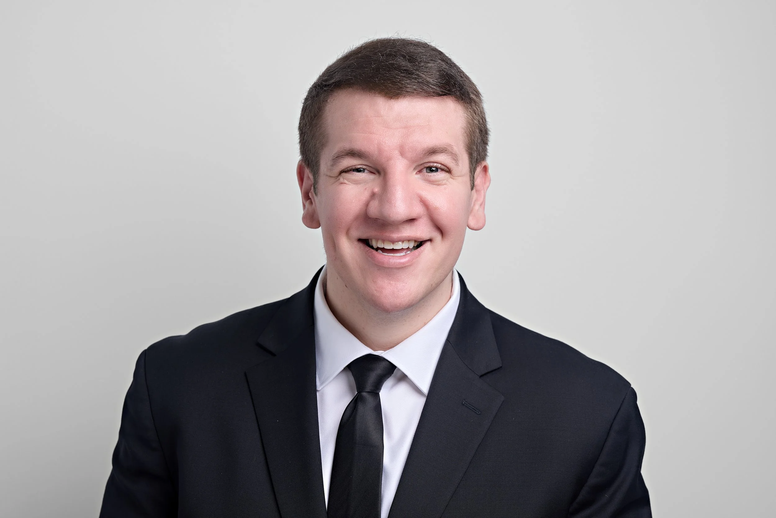 A smiling man in a dark suit and tie against a gray background