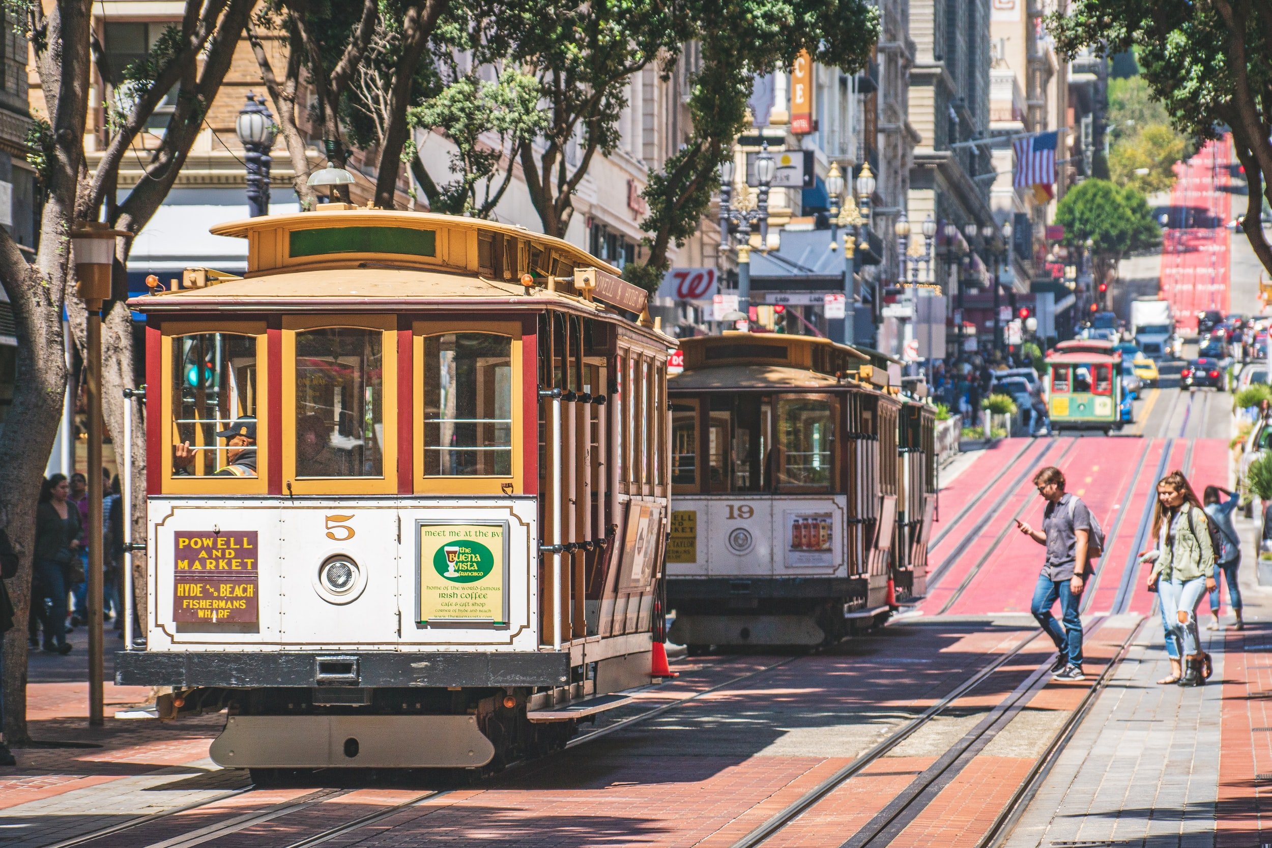 San Francisco cable cars on a busy street with pedestrians and buildings.