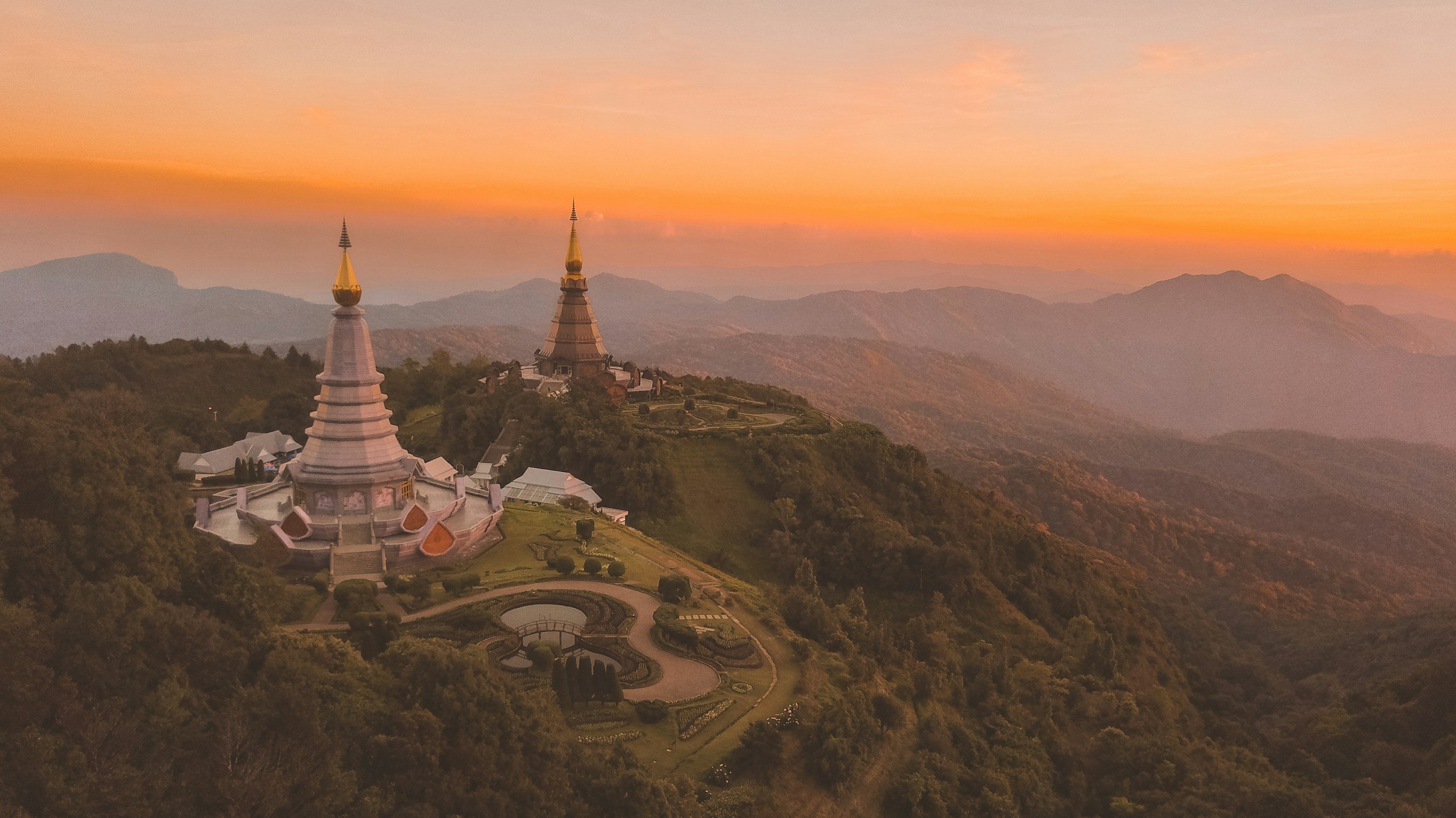 Sunset view of two pagodas on Doi Inthanon mountain with surrounding lush greenery and distant hazy mountains, Chiang Mai, Thailand.