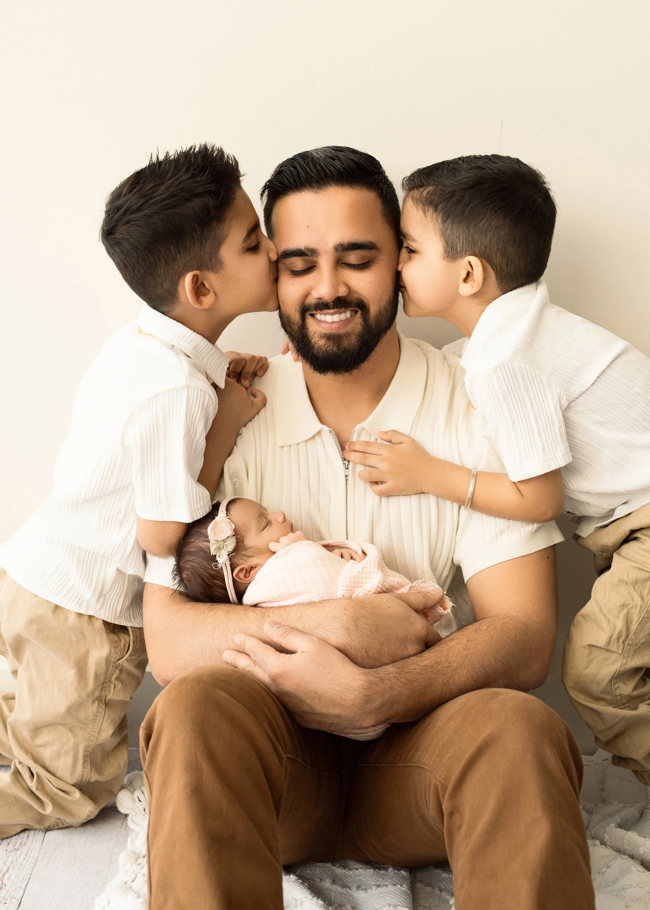 Sons kissing dad holding newborn