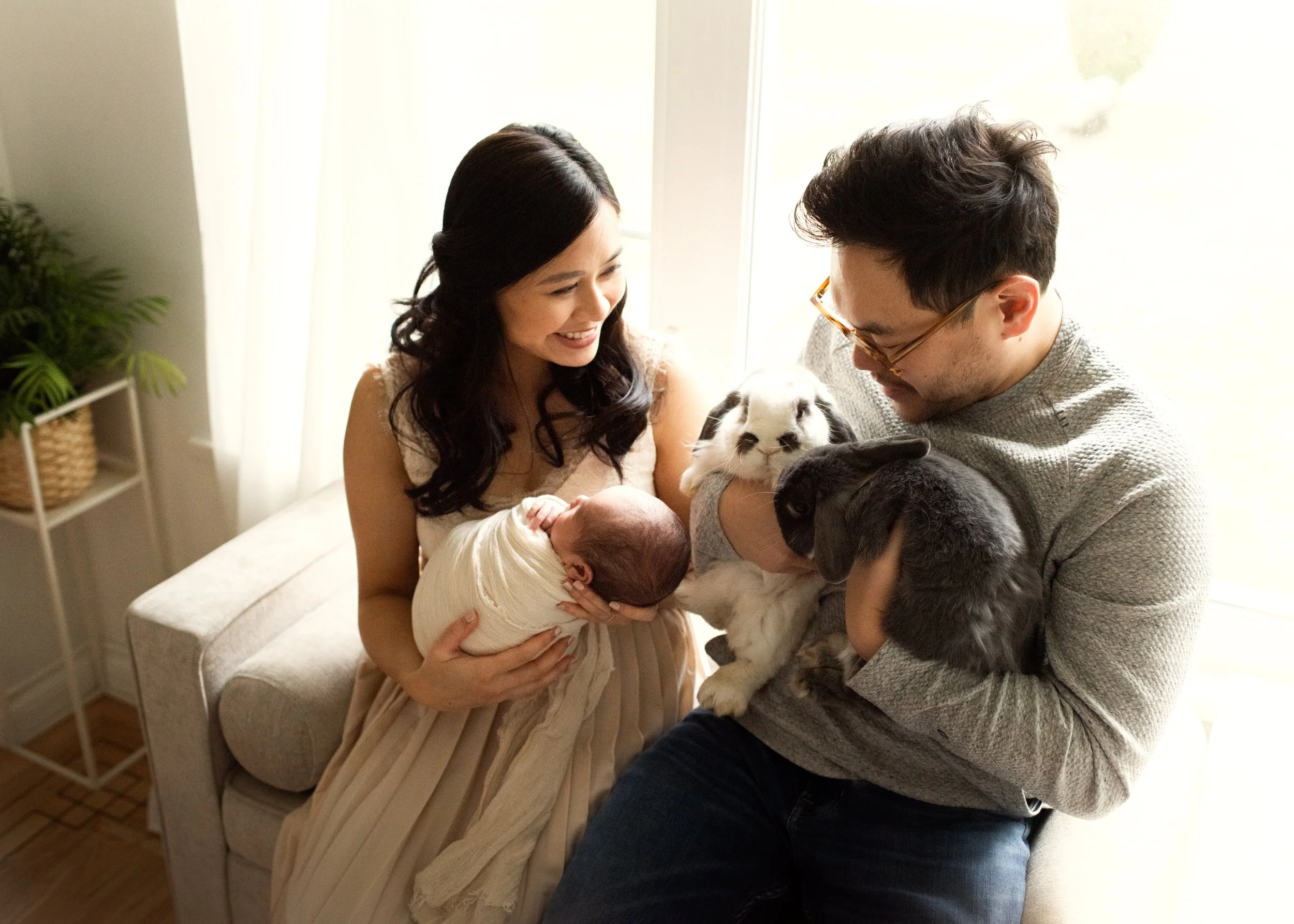 New parents holding newborn baby beside the window with two bunnies