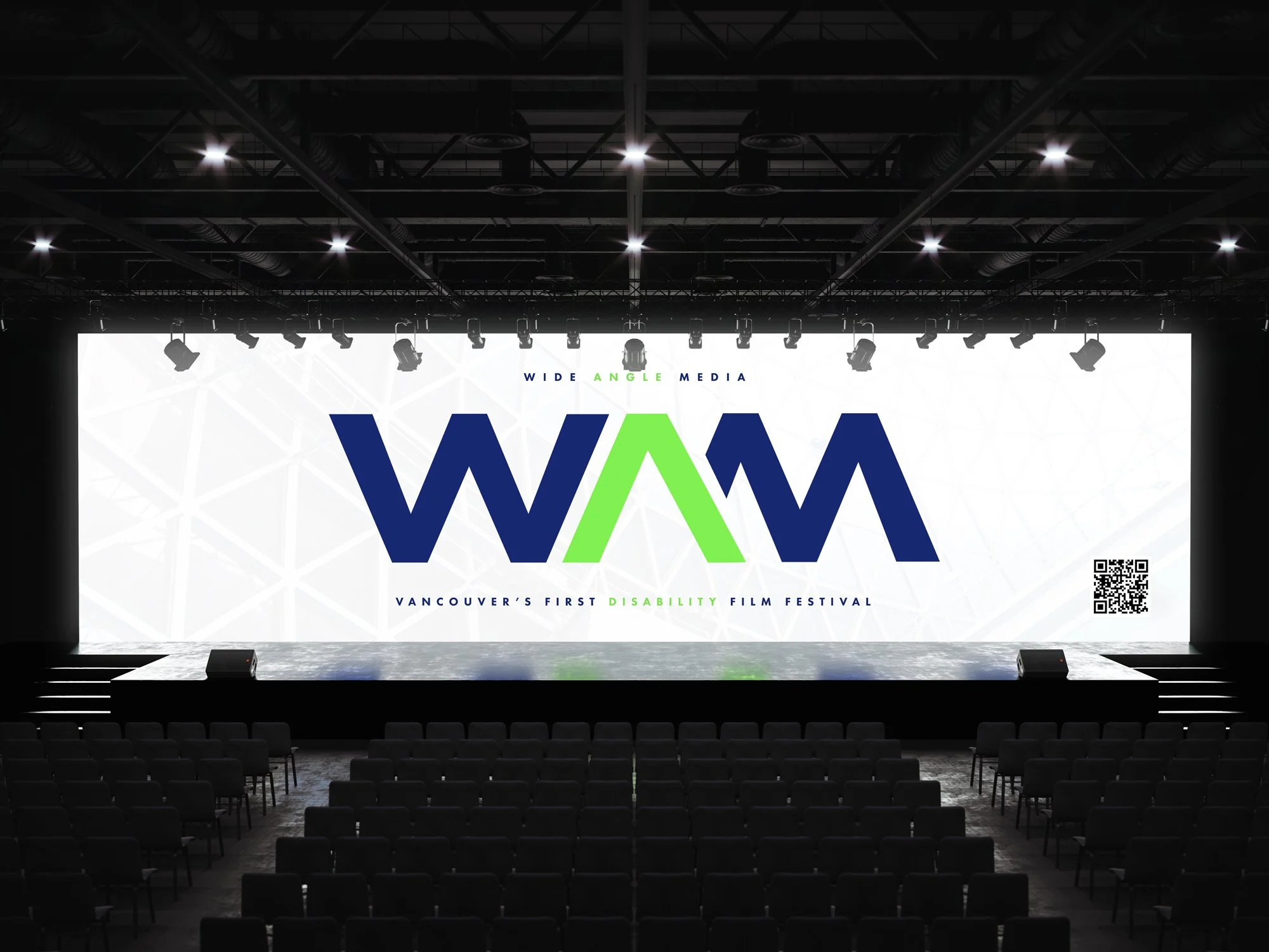 Large stage with a bright screen displaying the logo of VIFF, Vancouver's first disability film festival, in a dark theater setting with chairs and stage lighting.