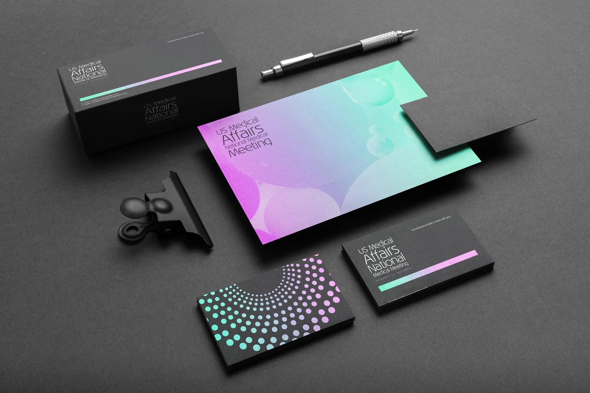 Collection of branding materials including a black box, brochures, business cards, a pen, a paperclip, and black paper, on a gray surface.
