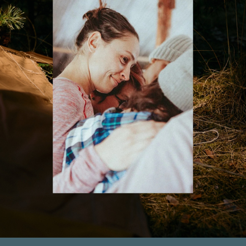 A woman and a man are cuddling and smiling, with the woman wearing a pink long sleeve shirt and the man wearing a gray beanie and a plaid shirt, in a warm, intimate moment indoors.