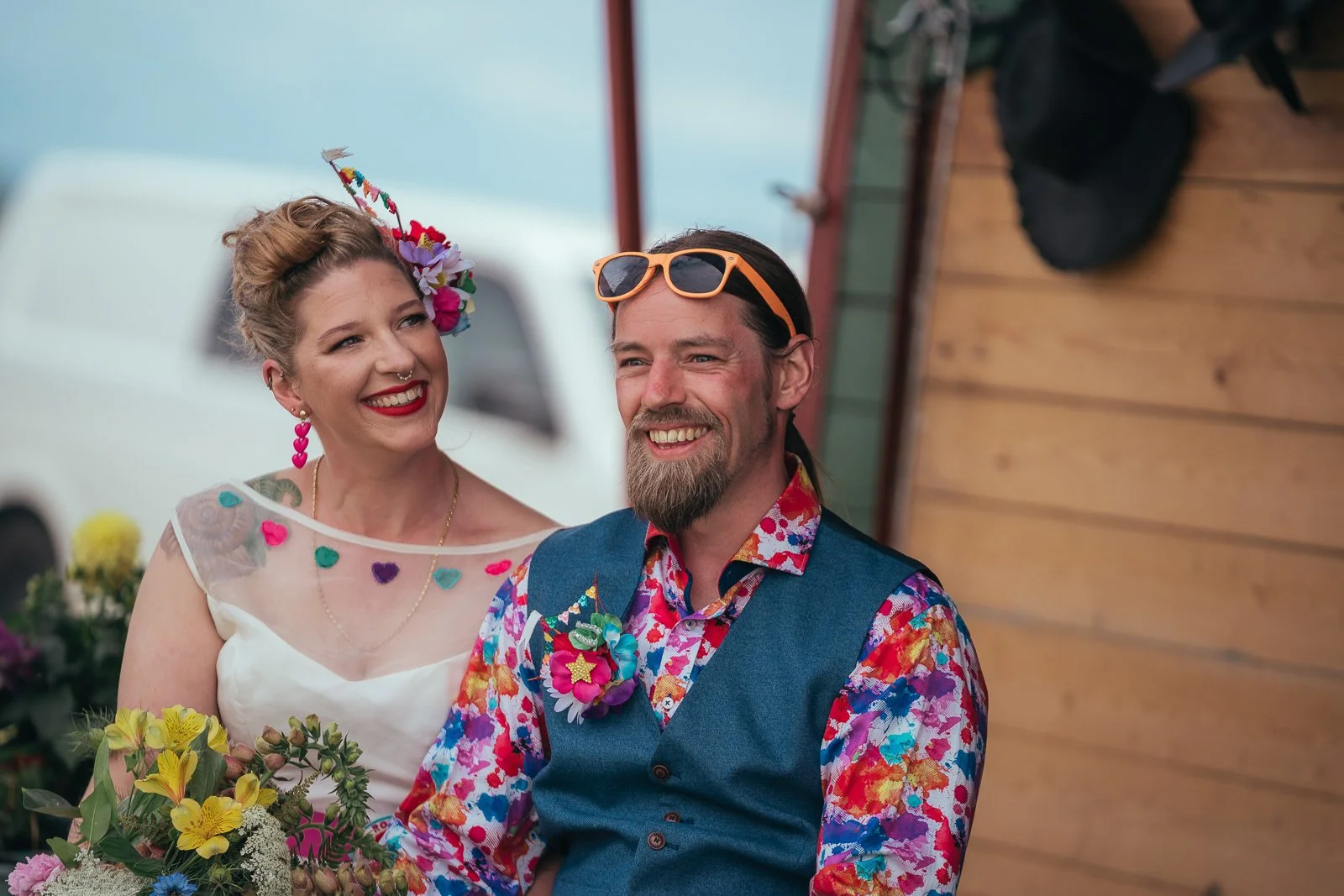 A smiling woman with colorful accessories and a man with sunglasses at an outdoor event.