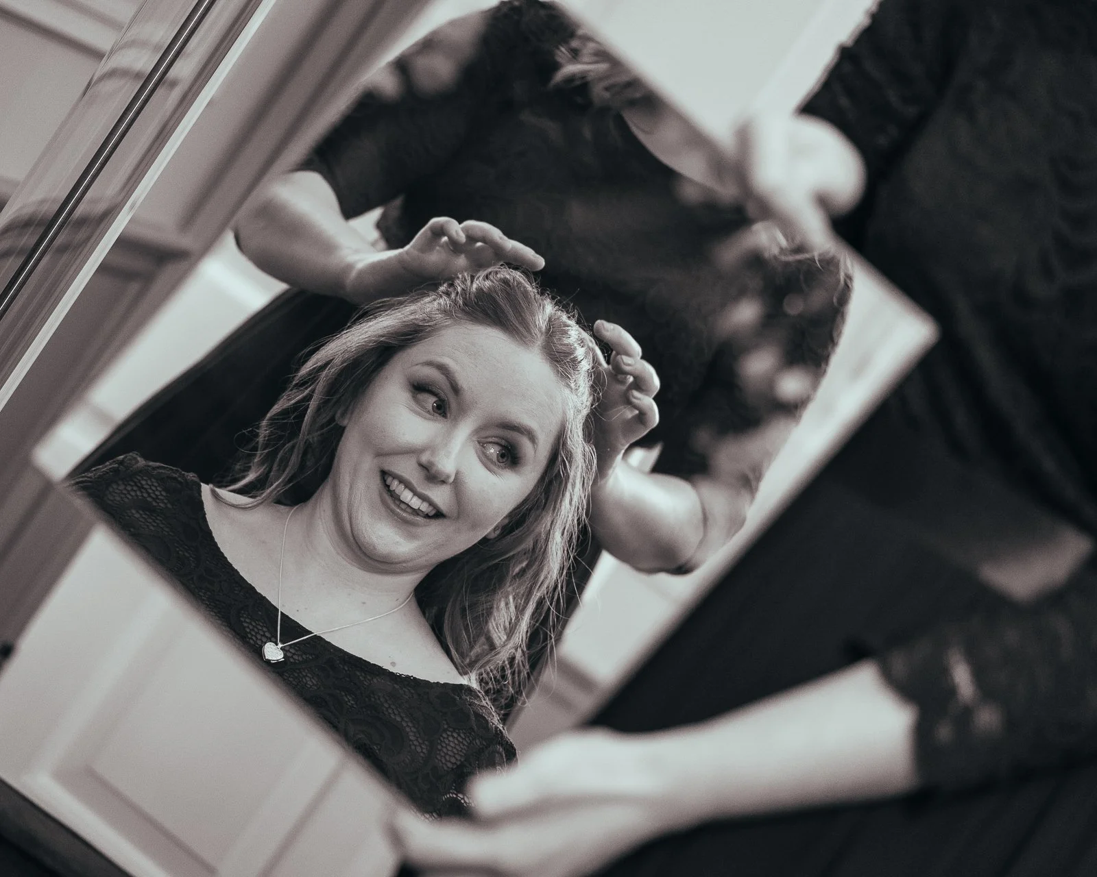 A woman smiling at her reflection in a mirror while a hairstylist does her hair.