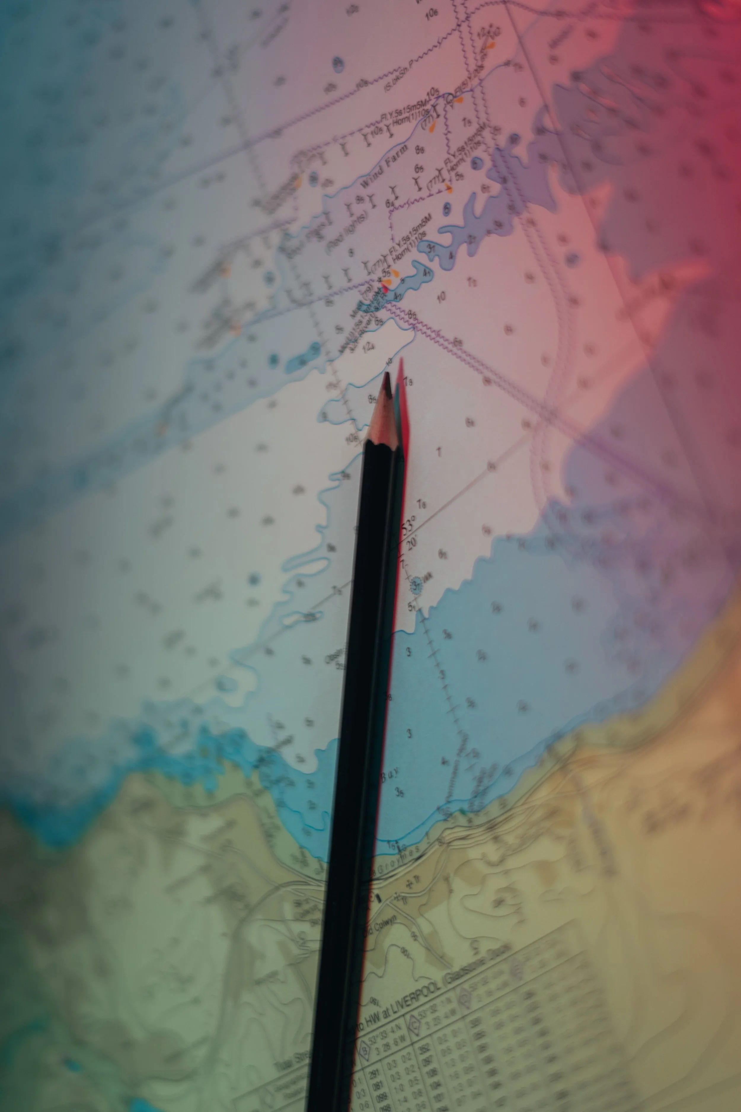 Close-up of a nautical chart with a pencil pointing at specific locations. The chart shows water depths, navigation routes, and land features near Liverpool.
