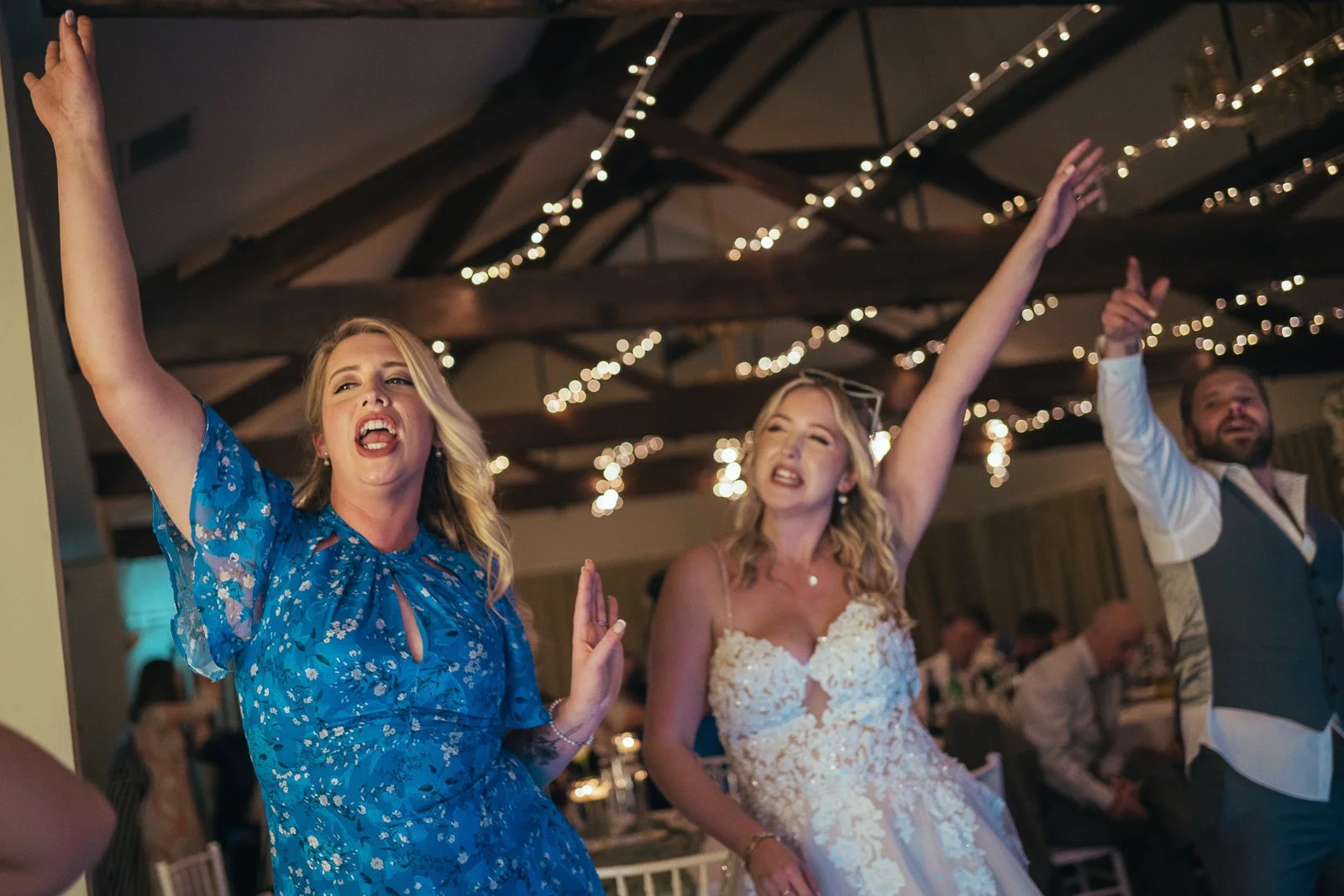 People celebrating at a wedding reception, dancing and enjoying the moment indoors with string lights hanging from the ceiling.