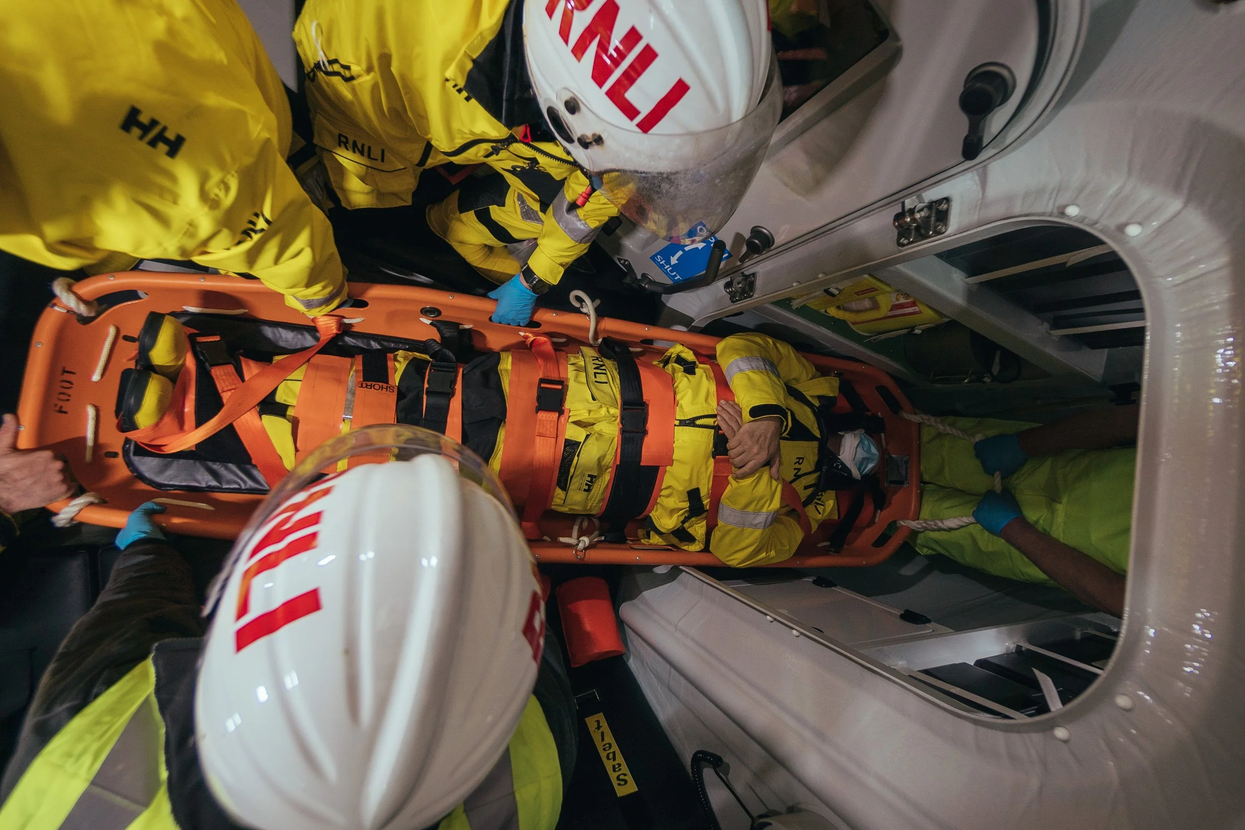 Emergency medical personnel in yellow uniforms and white helmets attending to a person lying on a stretcher inside an ambulance.