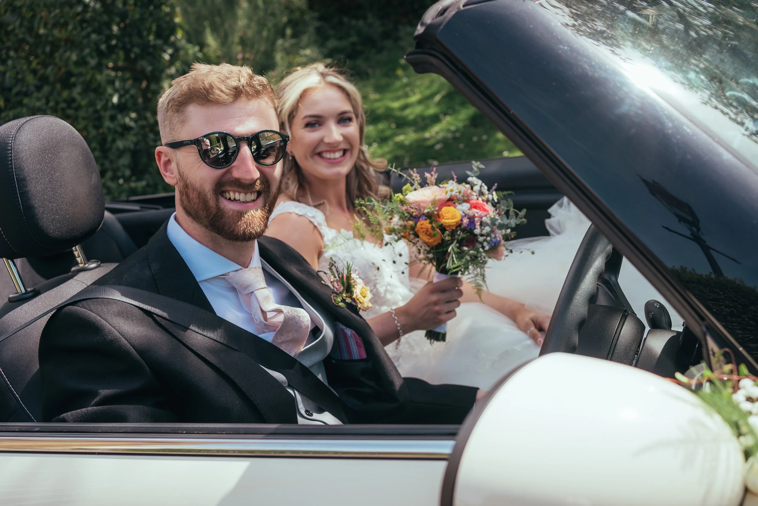 Bride and groom with bouquet in hand reading to drive off into newlywed life