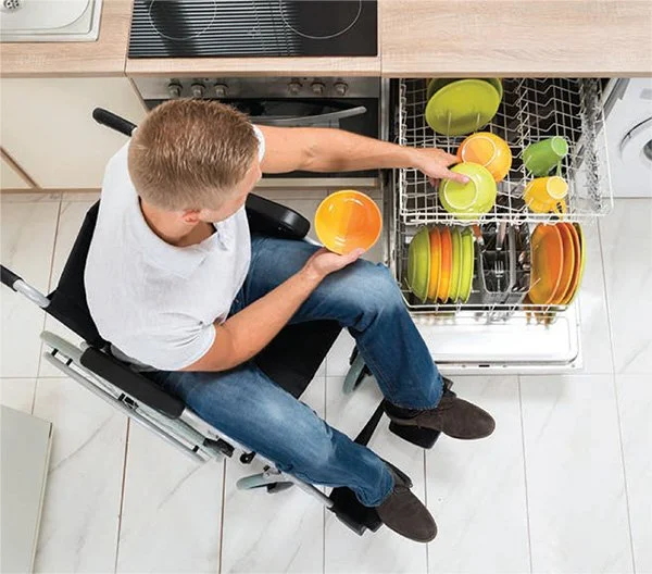 Young man sitting in a wheelchair, loading dishes into a dishwasher