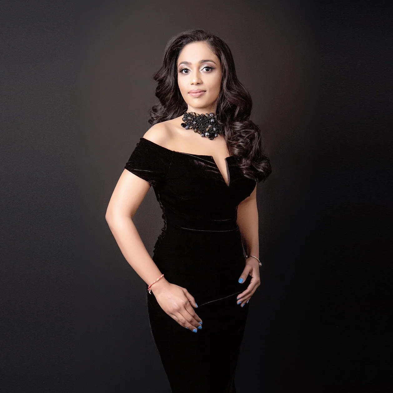 Elegant woman in black dress with jewelry, posing against a dark background.