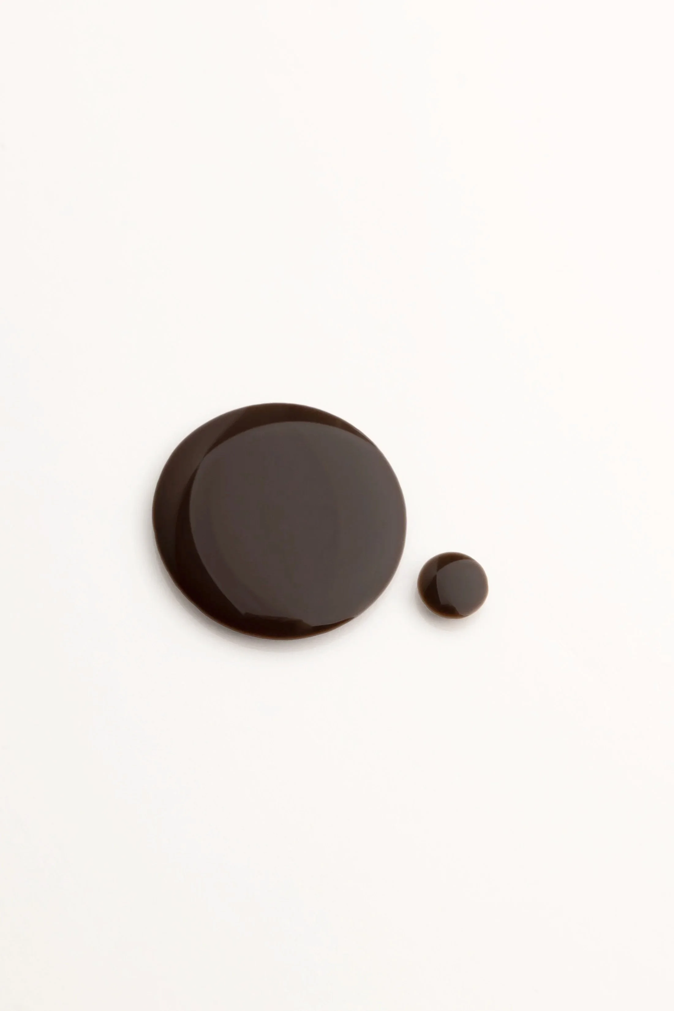 Three dark brown circular objects of varying sizes on a white surface, with the largest towards the lower left and two smaller ones nearby.