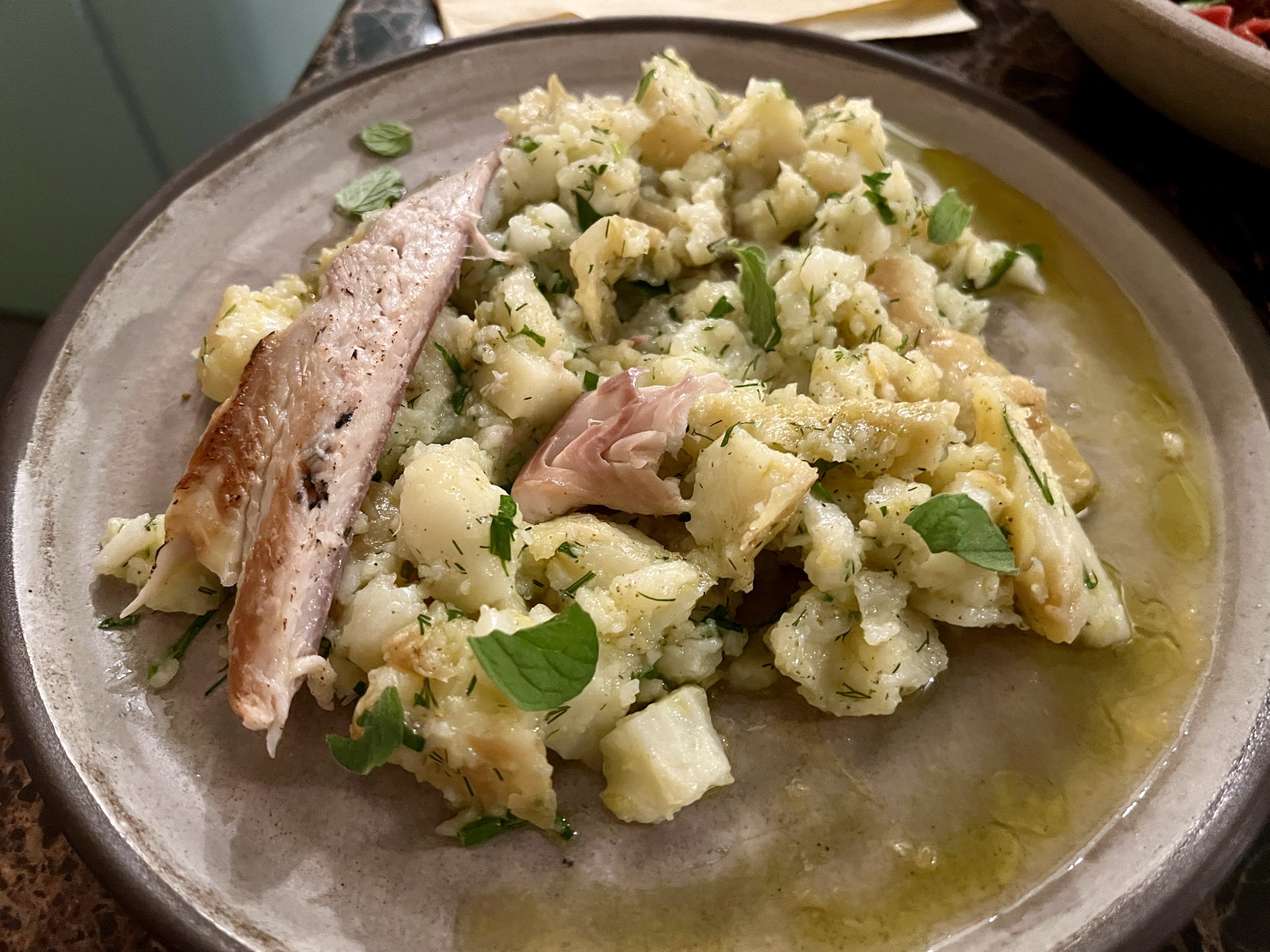 Kartoffelsalat mit Kräutern und gegrilltem Fisch auf einem Teller.
