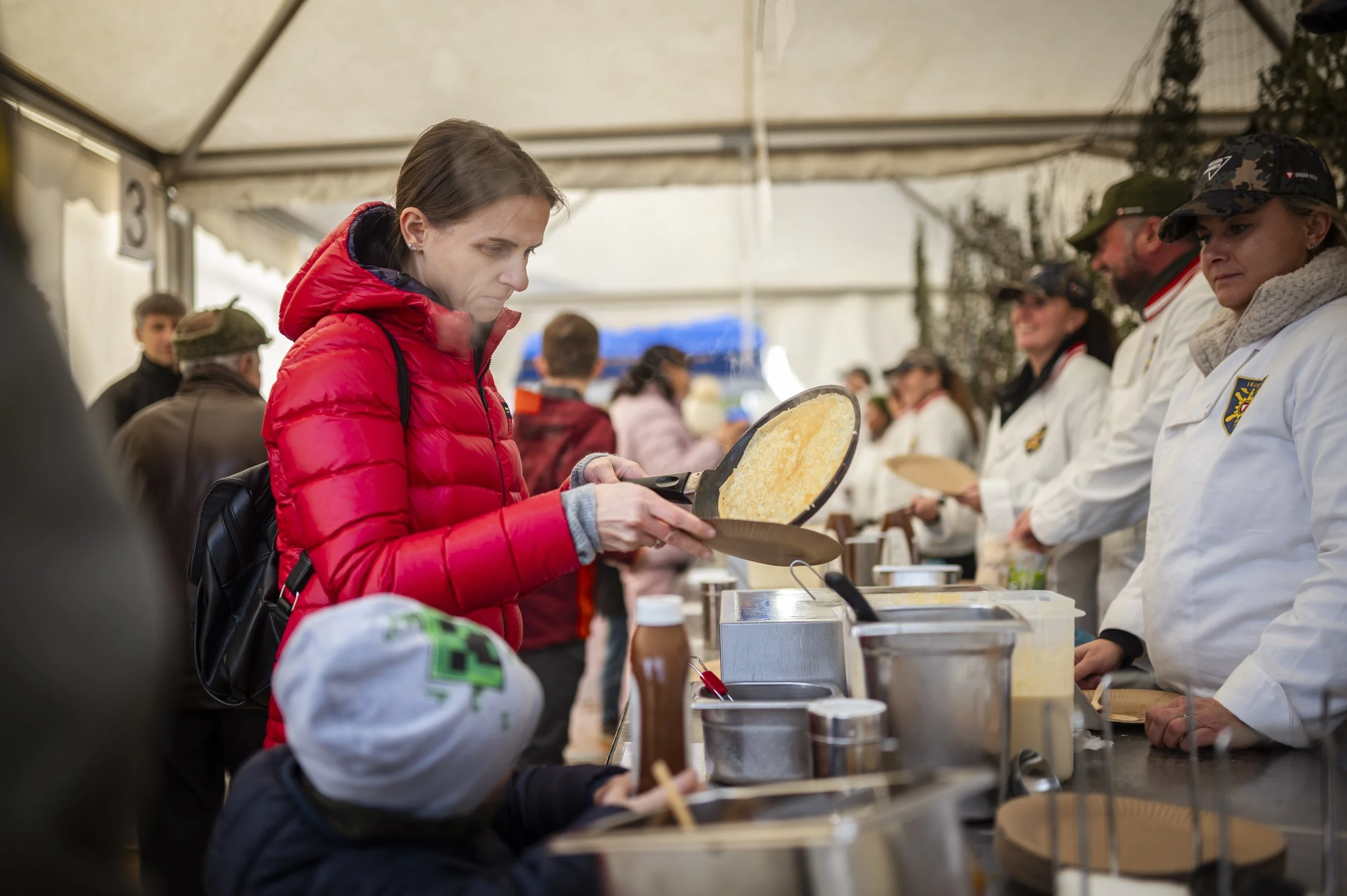 Menschen beim Essen in einer Zeltveranstaltung, einige in weißen Kochjacken.