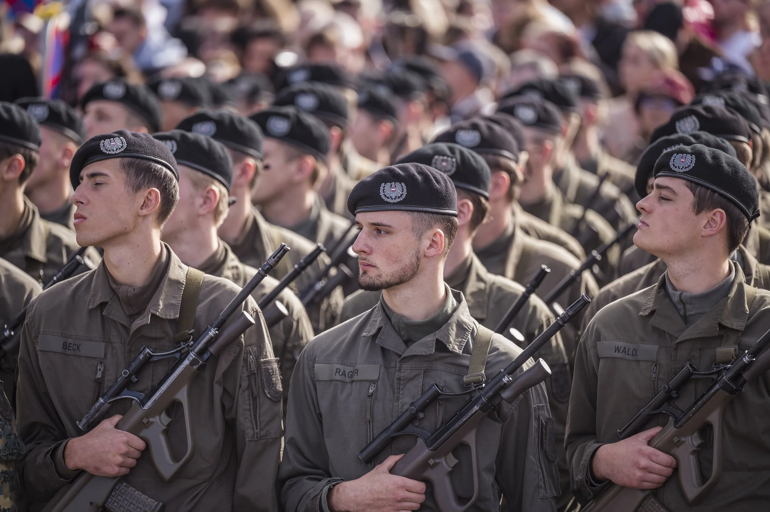 Soldaten in Uniformen und Mützen mit Abzeichen stehen in einer Reihe im Freien.