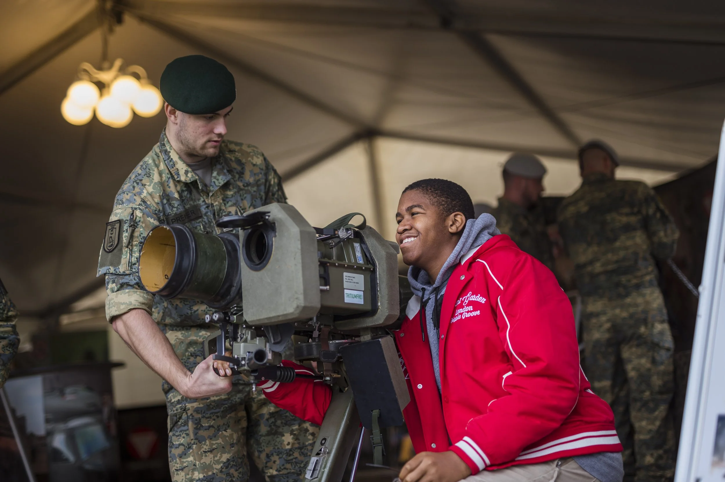 Soldat und junger Mann bedienen eine Filmkamera in einem Zelt, im Hintergrund weitere Soldaten in Tarnuniform.