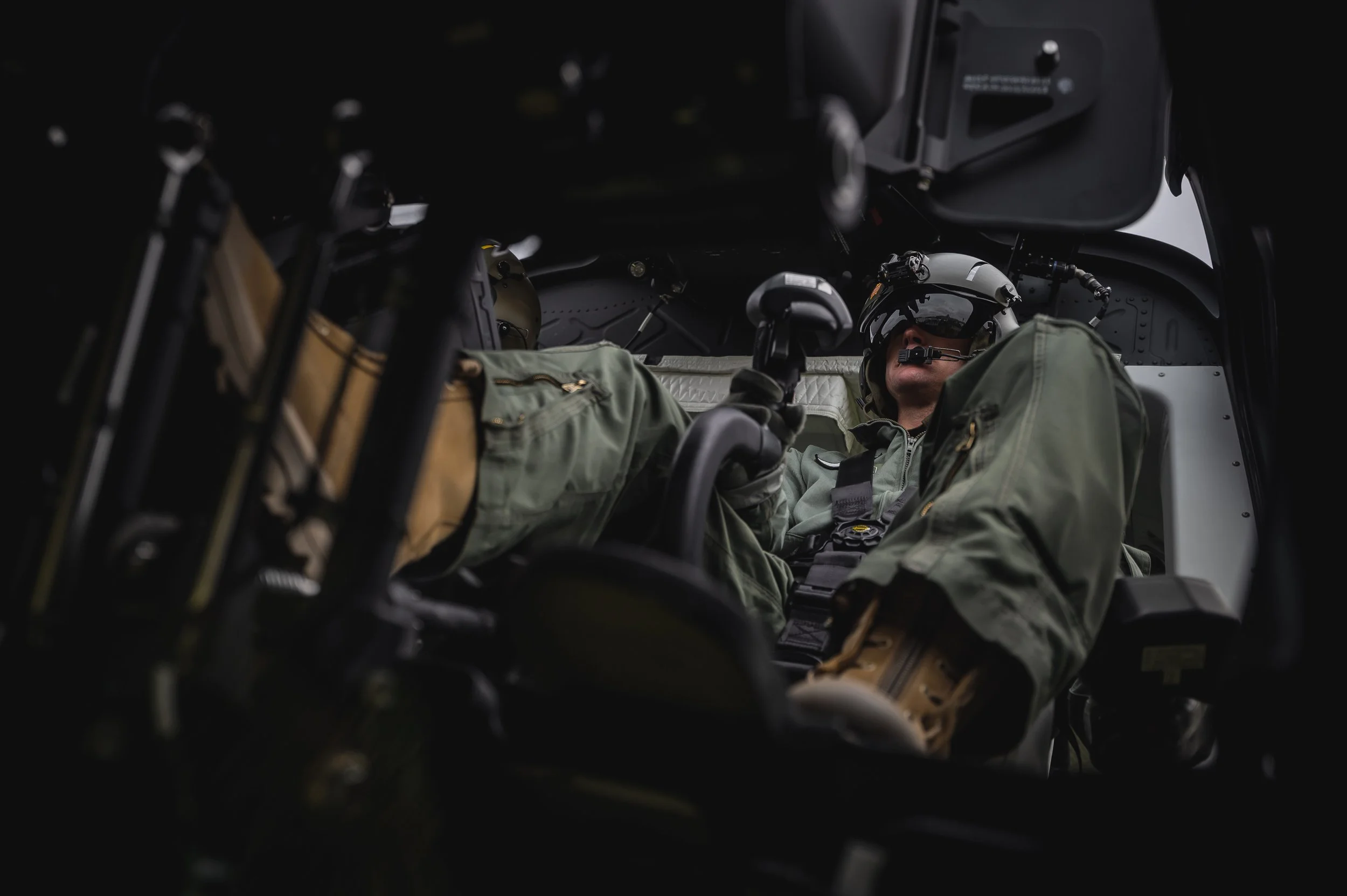 Ein Soldat sitzt in einem militärischen Hubschrauber, trägt eine Schutzbrille und Kampfrüstung.