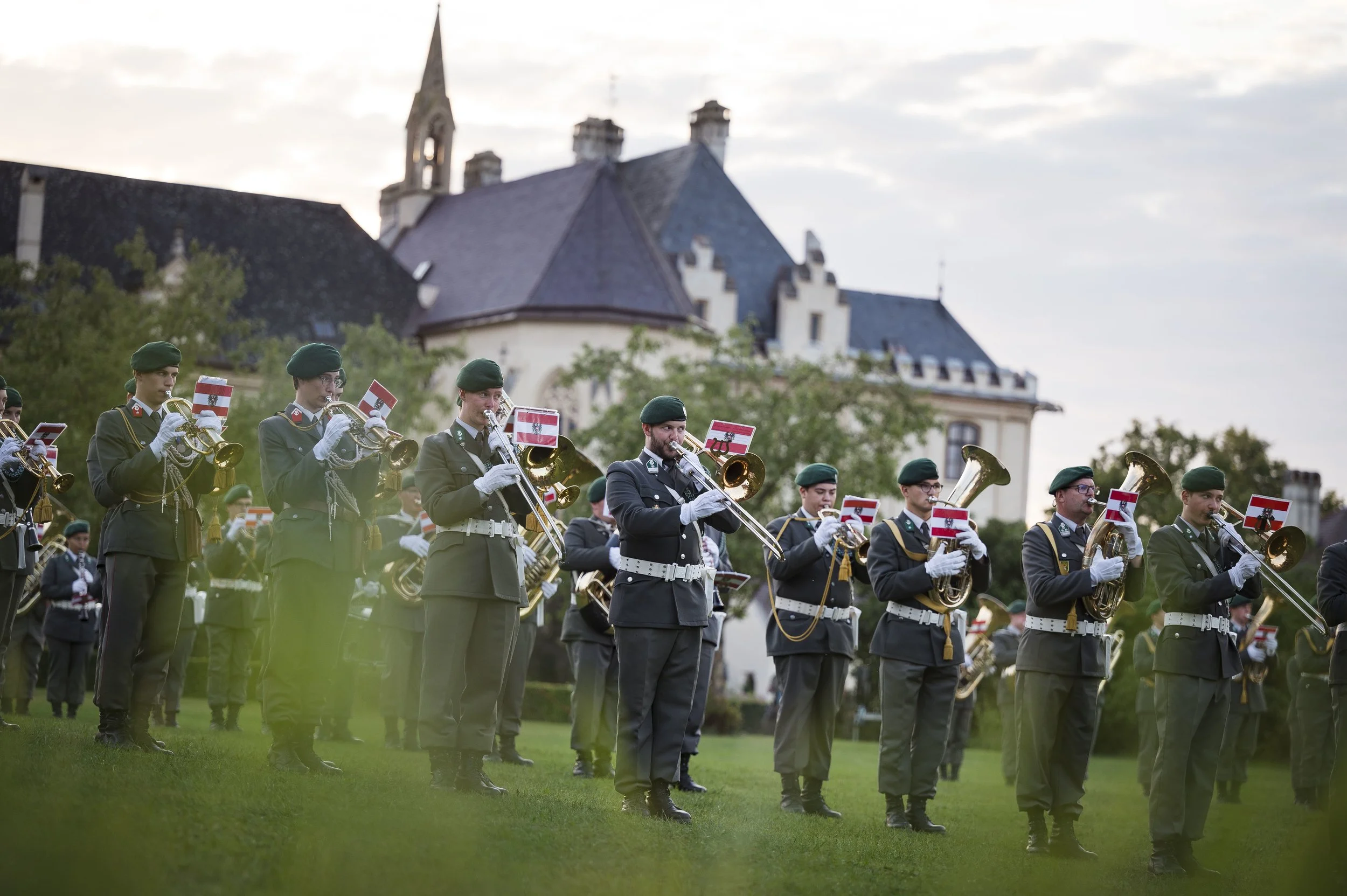 Eine Gruppe von Soldaten in Uniform spielt im Freien Musikinstrumente, getragen von einer musikalischen Parade, mit historischen Gebäuden im Hintergrund.