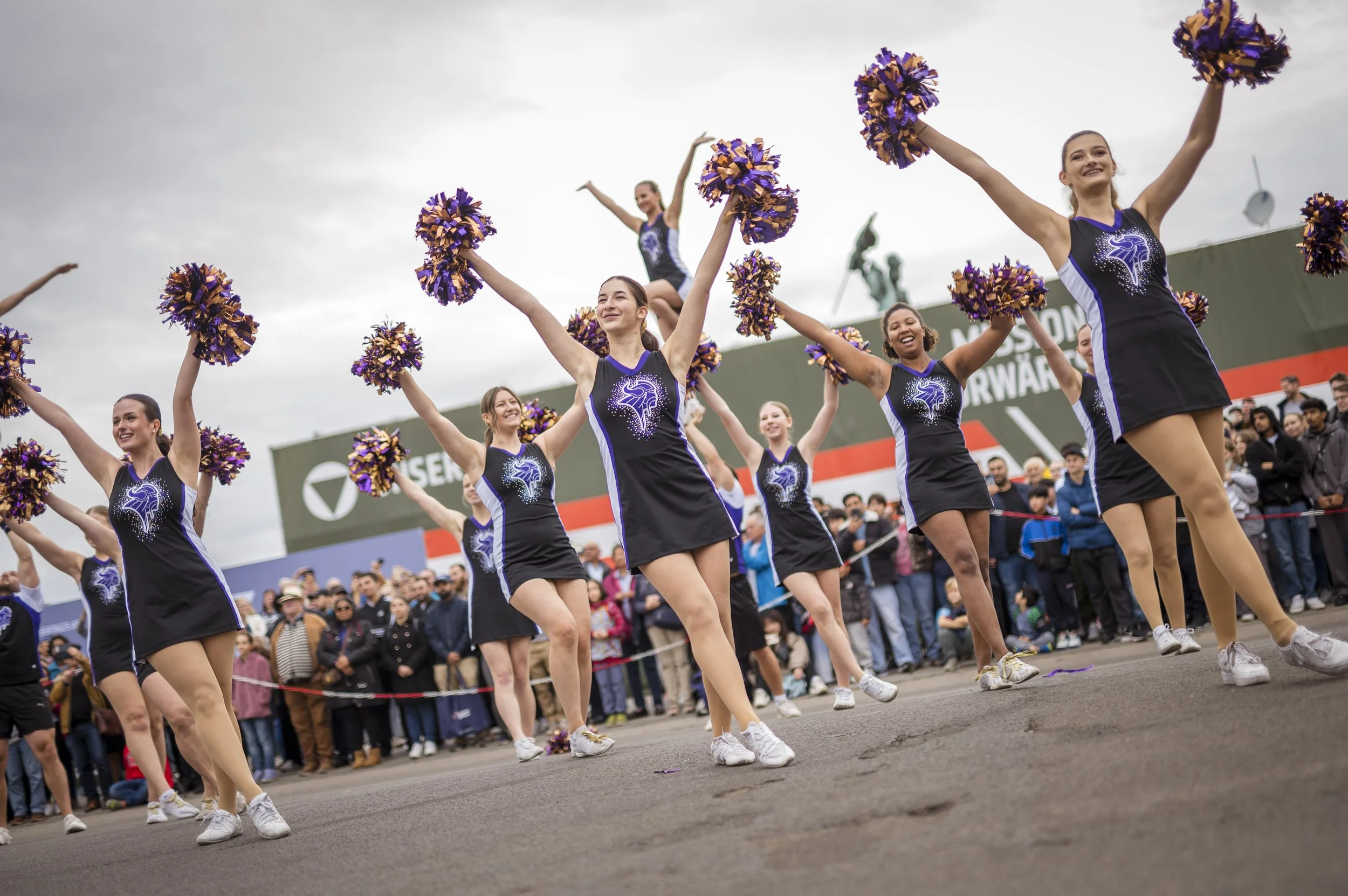 Mädchen im Cheerleader-Outfit beim Tanzen während einer Parade vor Publikum an einem bewölkten Tag.