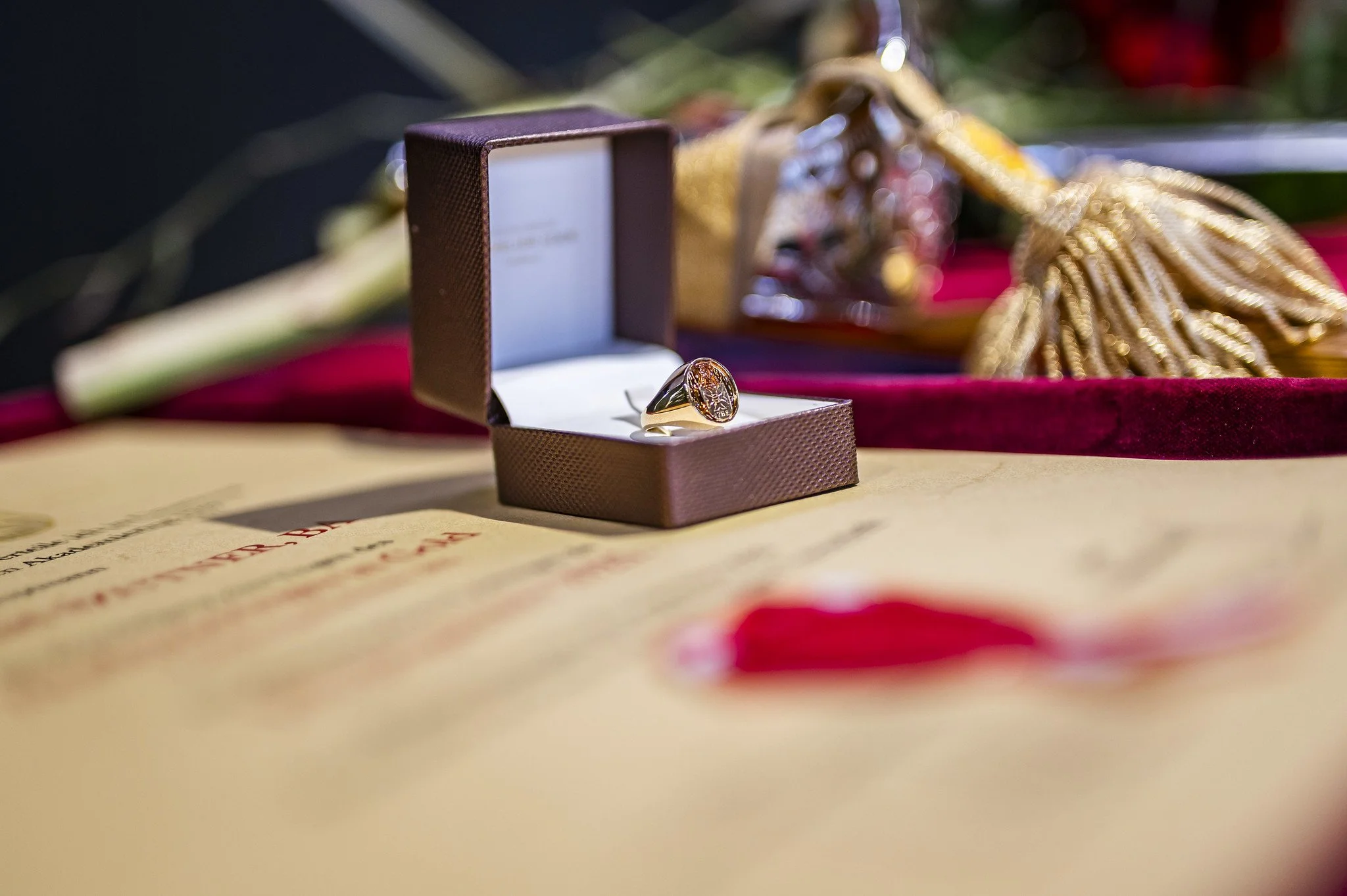 Goldener Ring in einer braunen Schmuckschatulle, im Hintergrund rote und goldene Dekorationen.