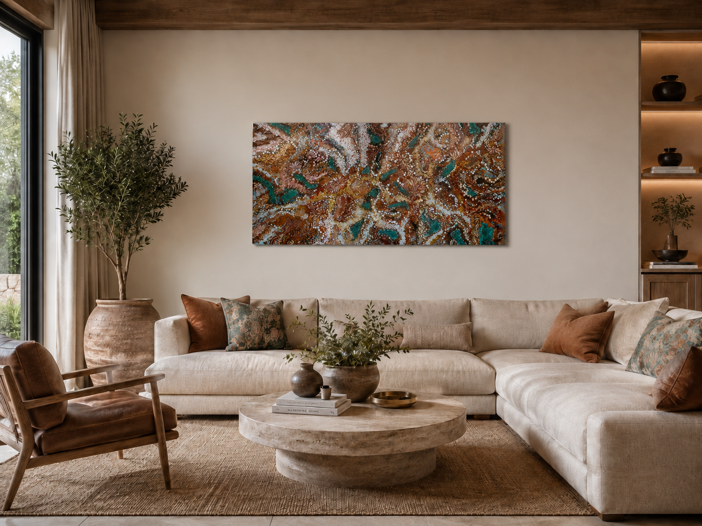 Living room with large beige sectional sofa, decorative pillows, a round marble coffee table with vases and books, a plant in a large clay pot, an abstract colorful painting on the wall, a brown leather armchair, and built-in shelves with decorative 