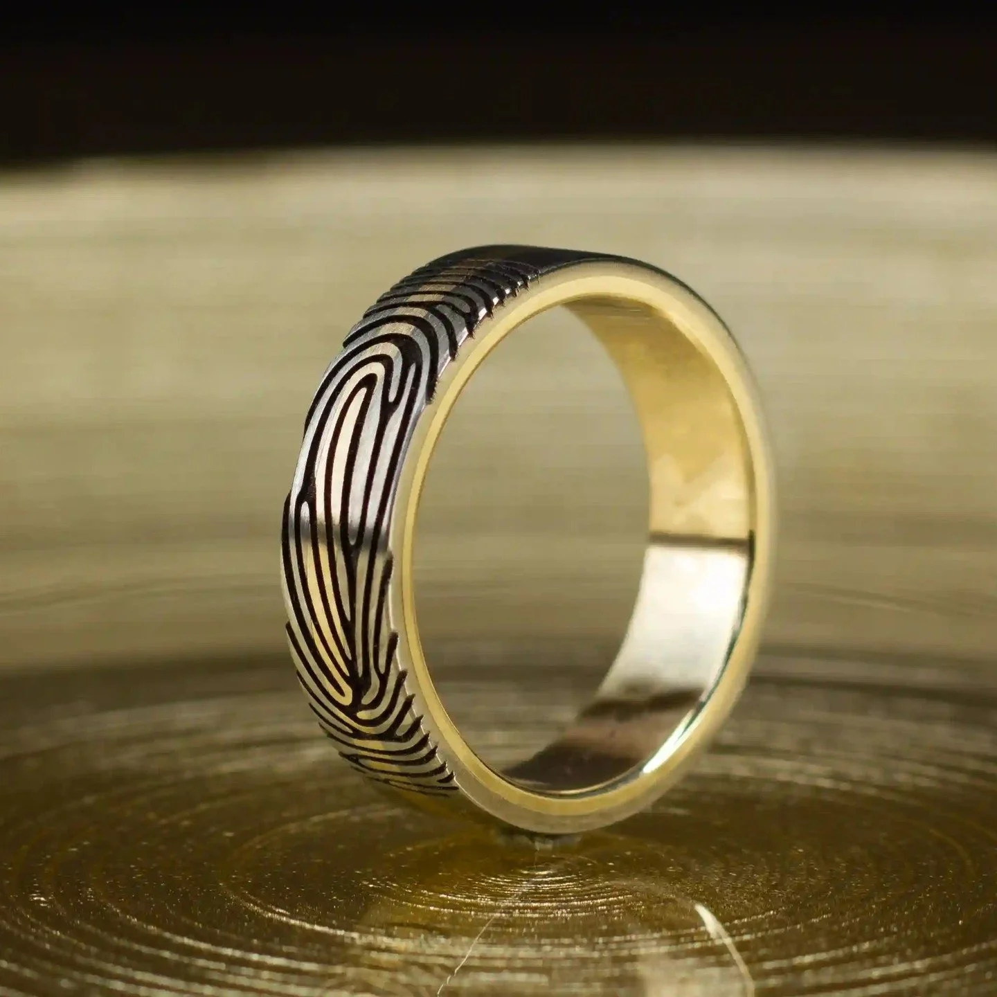 De kracht van titanium. De warmte van geelgoud. De ziel van een vingerafdruk.

Deze ring bestaat uit twee titanium buitendelen, een massieve gouden middenband en een geelgouden binnenzijde. De buitenzijde draagt een persoonlijke vingerafdruk, vereeuw