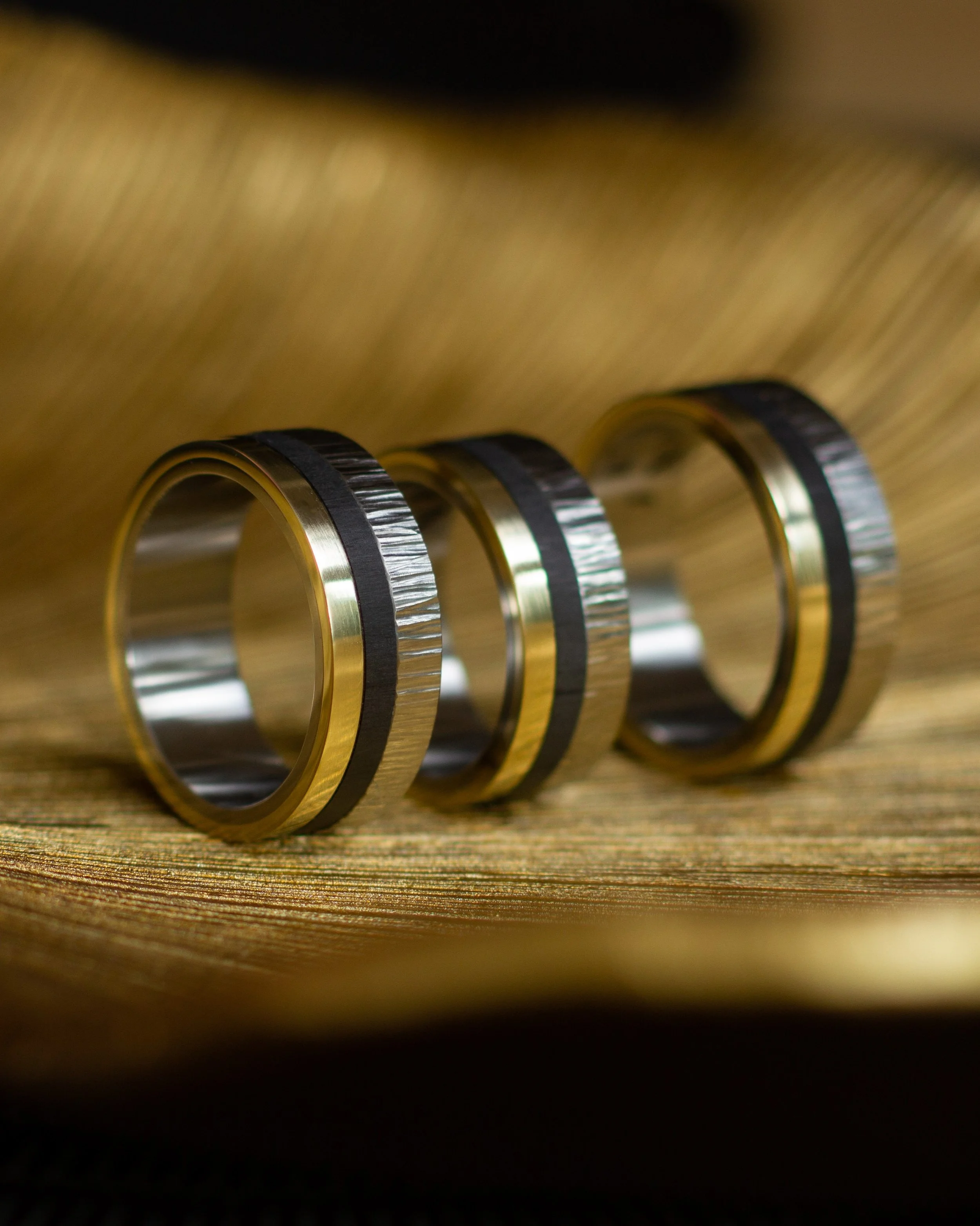Drie ringen. E&eacute;n familie. E&eacute;n verhaal.

Vervaardigd uit titanium met een handgesmede hamerslagstructuur, een strakke carbonlijn en een band van 14 karaat geelgoud.

Drie materialen. Titanium, carbon en goud.
Voor mij een mooie symboliek