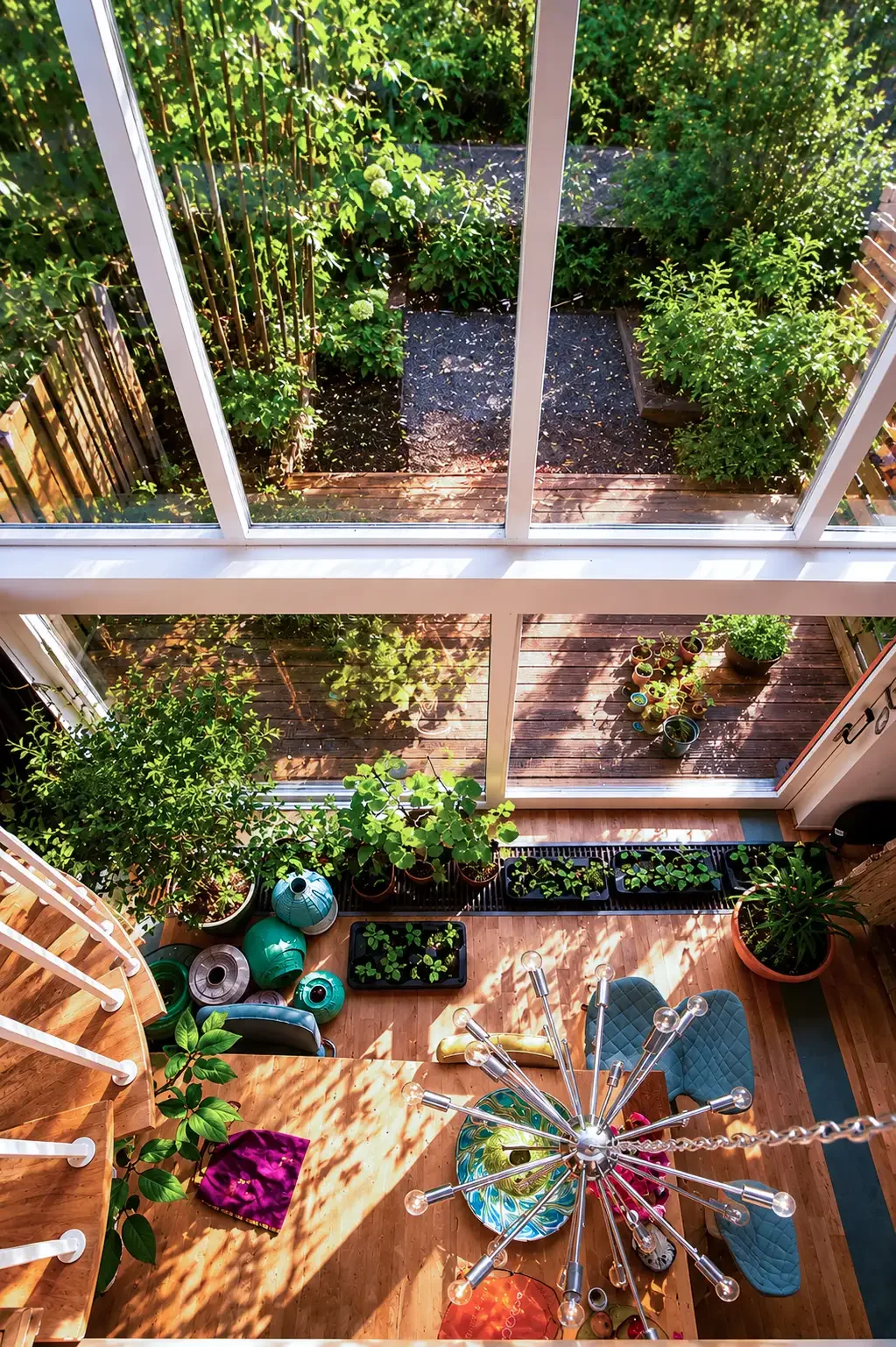 Een binnenruimte met een houten vloer, planten en tuingerei, uitzicht op een tuin met een houten terras, groene struiken en planten. rustige ontvangst ruimte.