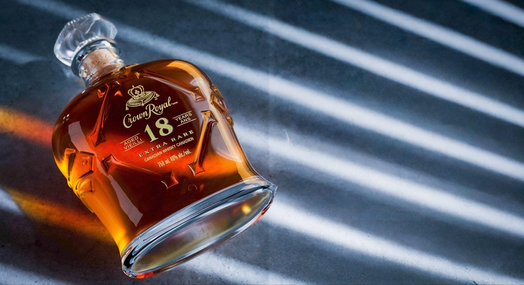 A bottle of Crown Royal 18-year-old Canadian whiskey lying on a surface with diagonal light shadows.
