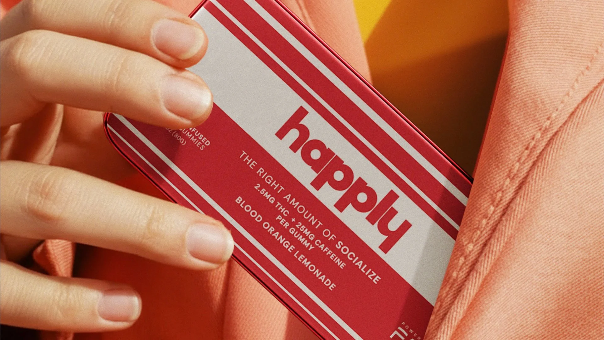 A hand holding a red and white box of superfood gummies called 'happily'. The box mentions ingredients like THC, caffeine, blood orange, and lemonade flavor.