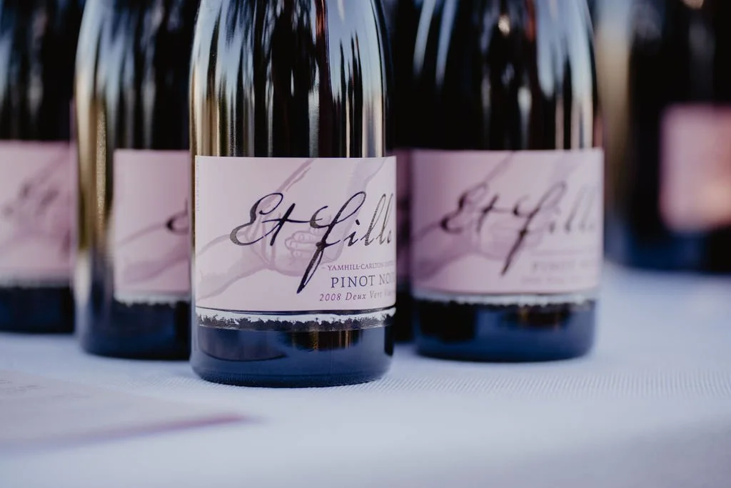 Multiple bottles of Et Fille wine, featuring a pink label with cursive writing, placed on a white surface.