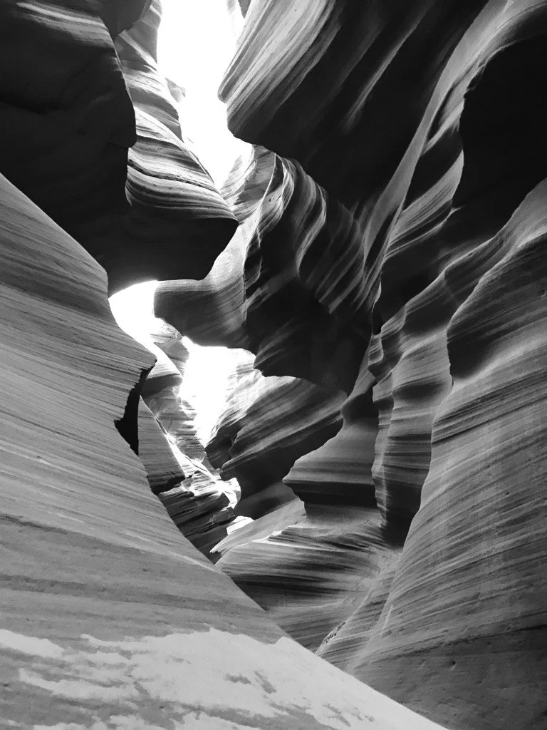 Black and white photo of a narrow canyon with smooth, layered rock walls forming winding passageways.